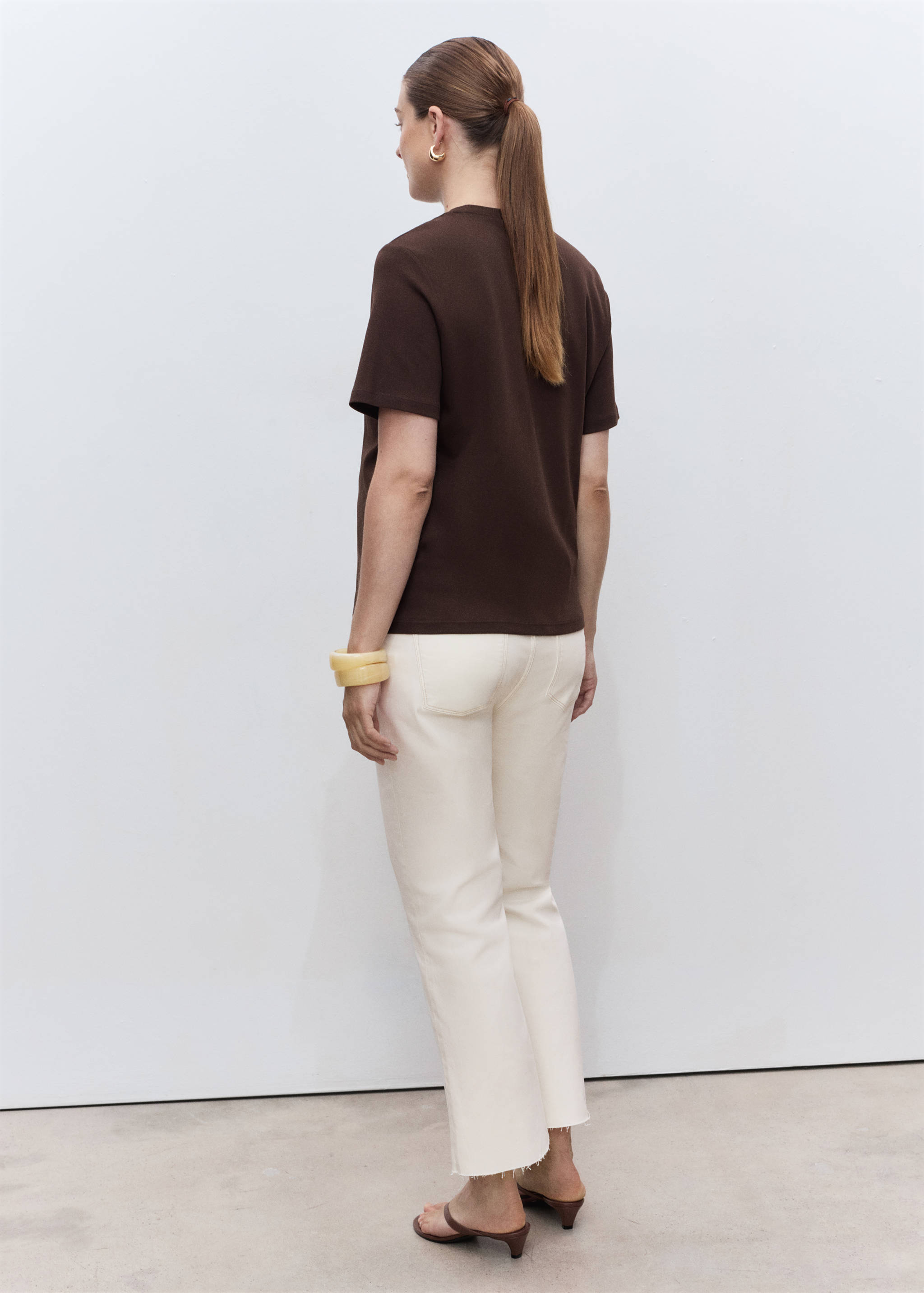 Back view of off-white trousers with raw hem, worn with a brown t-shirt.