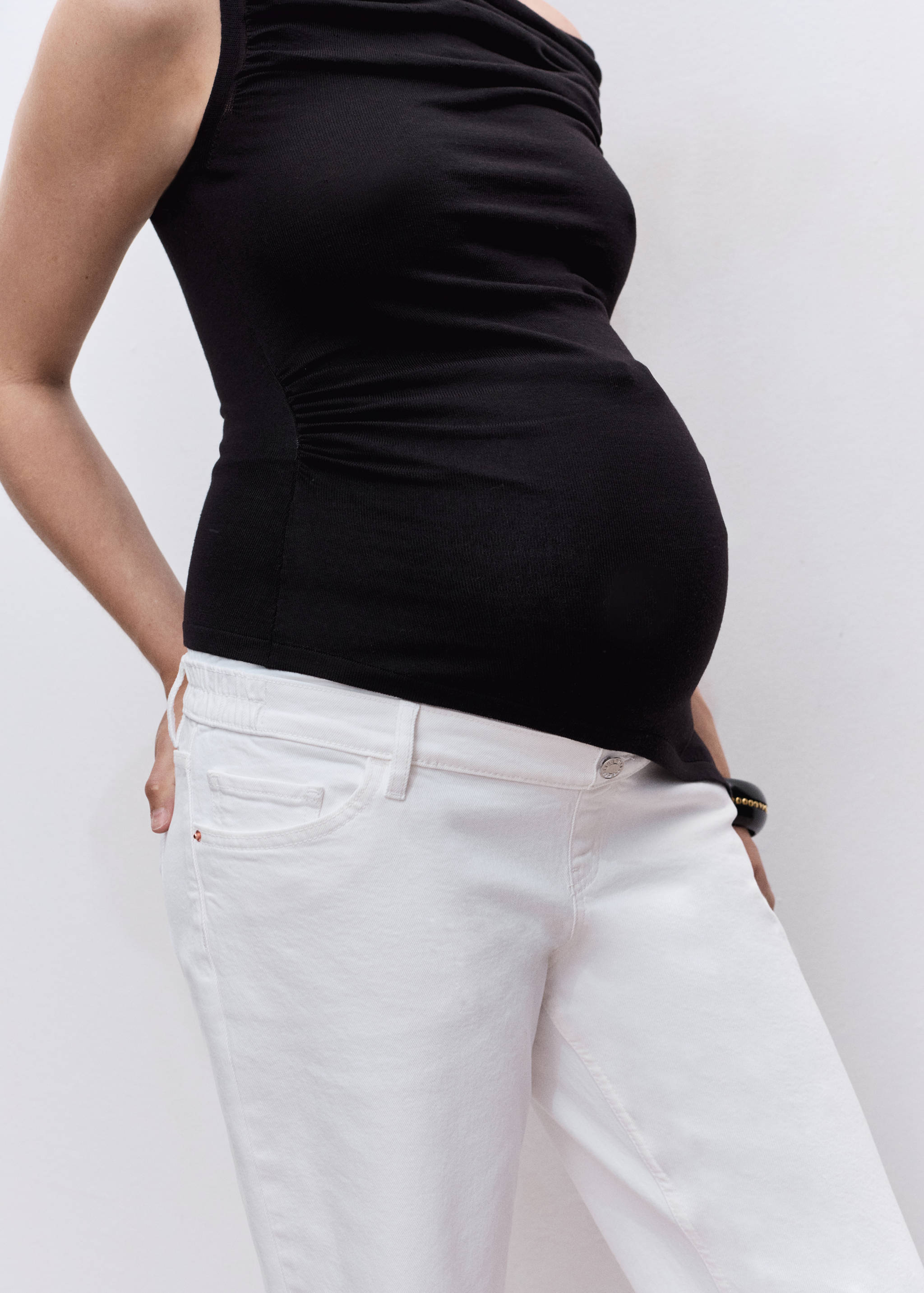 White denim trousers with a button fastening worn with a black top.