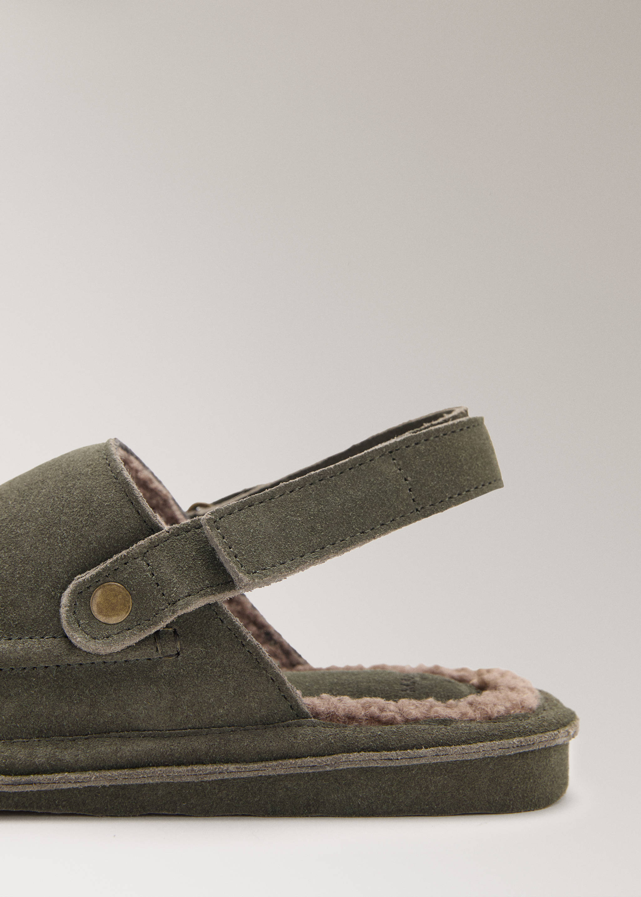 Close-up of olive green suede slippers with slingback strap and faux-fur lining.