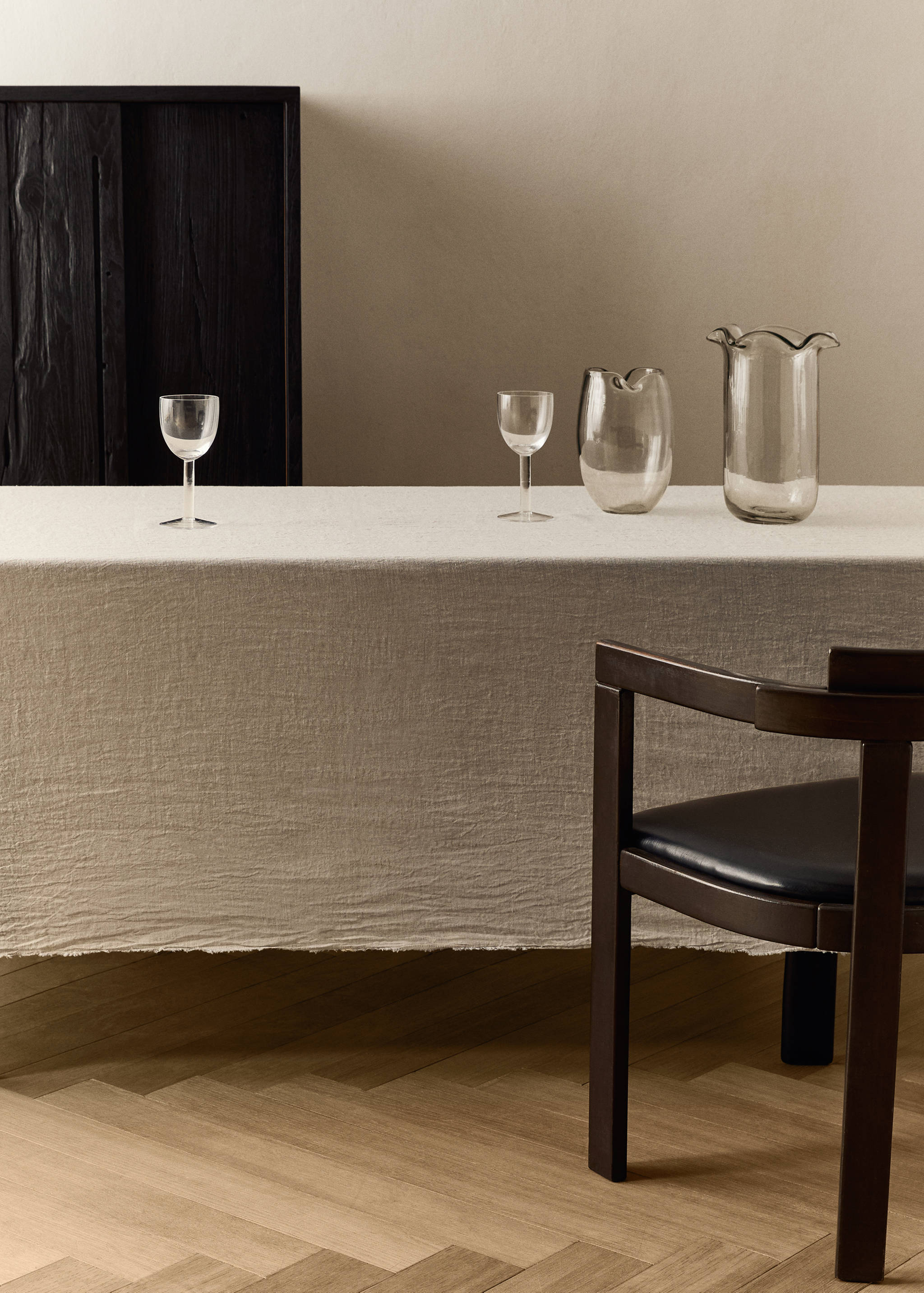 Beige tablecloth on a dining table with glassware and a wooden chair.