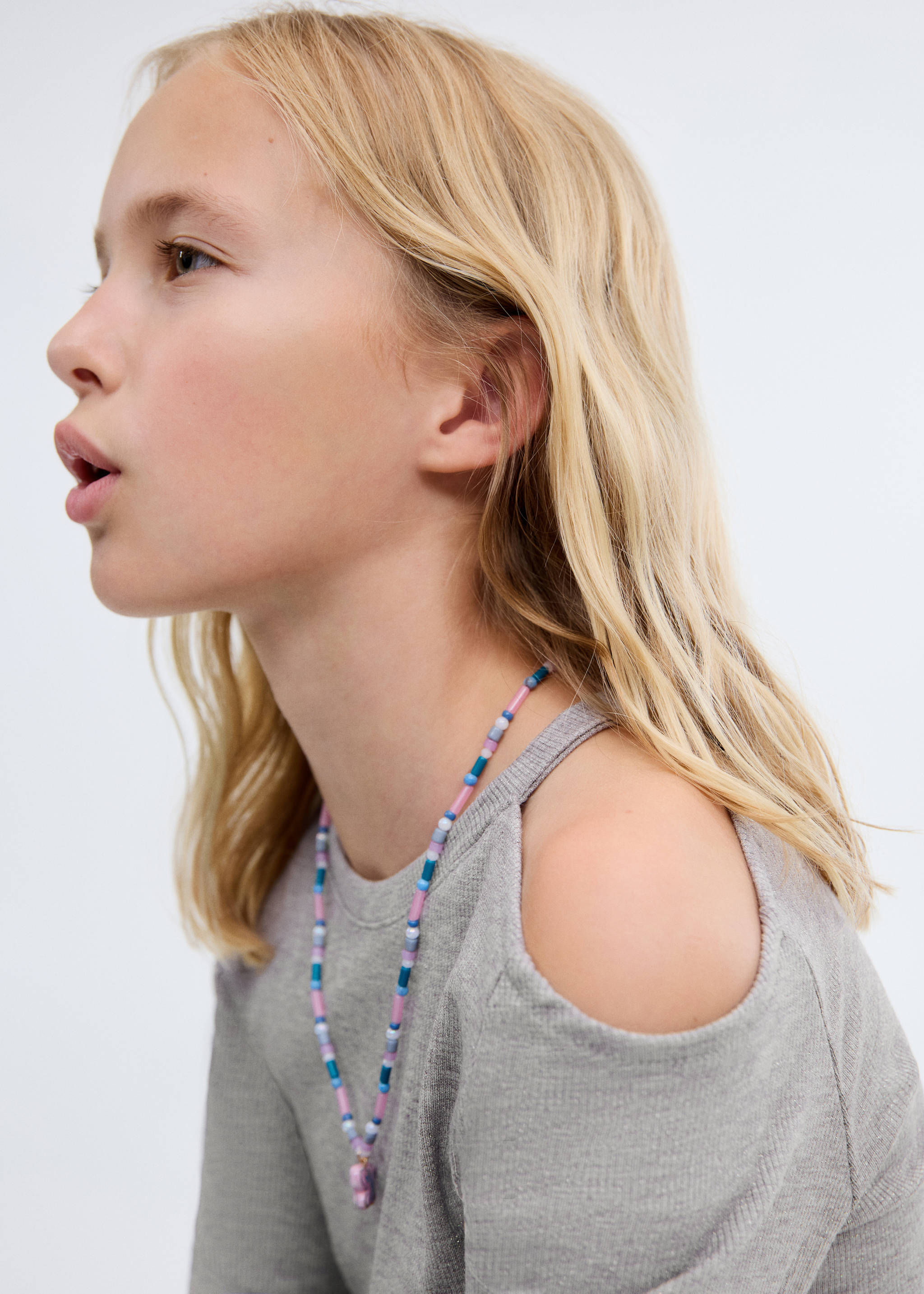 Grey ribbed t-shirt with cold-shoulder cutouts worn with a beaded necklace.