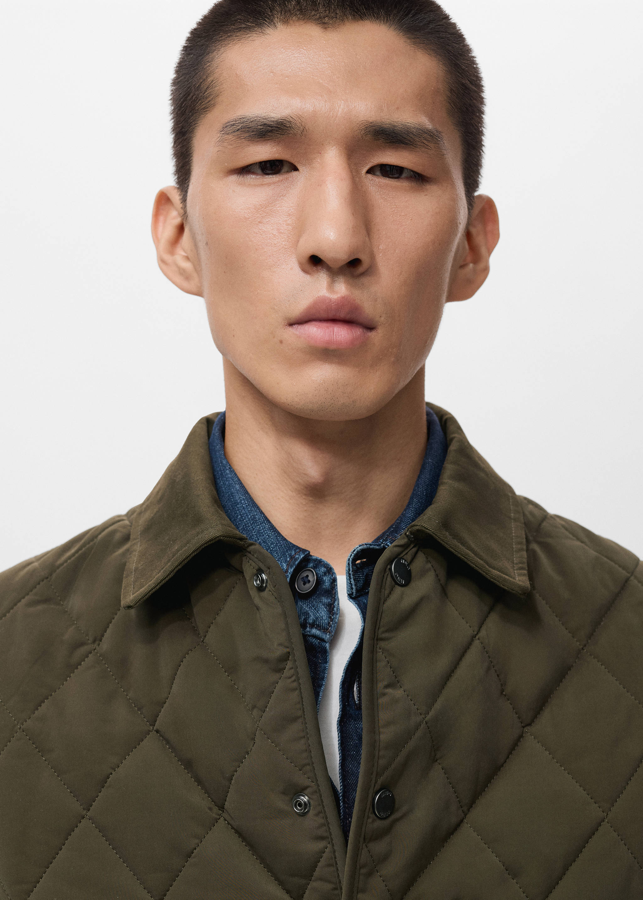 Close-up of an olive green quilted jacket with a collar and snap buttons.