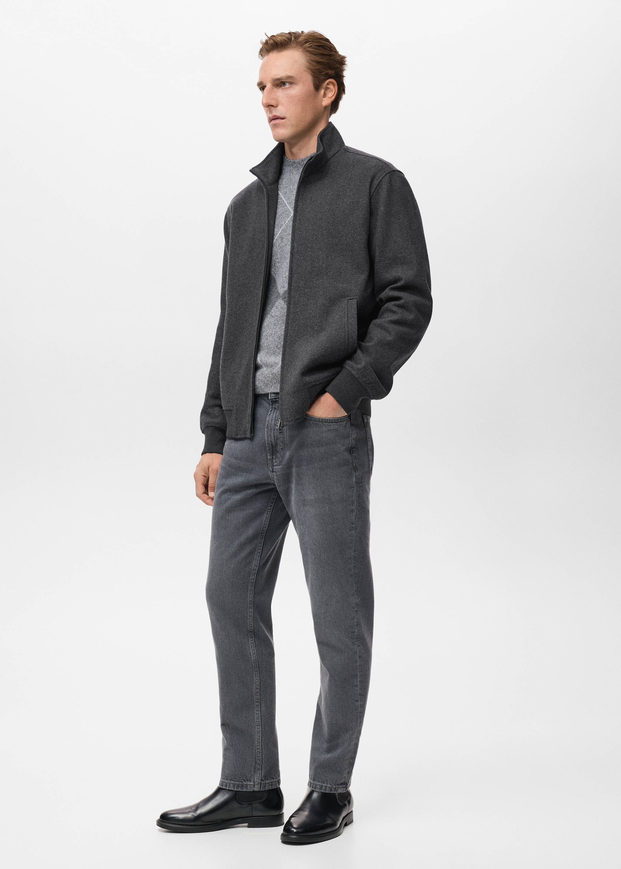 Dark grey zip-up sweatshirt with a high collar, worn with a patterned sweater and trousers.