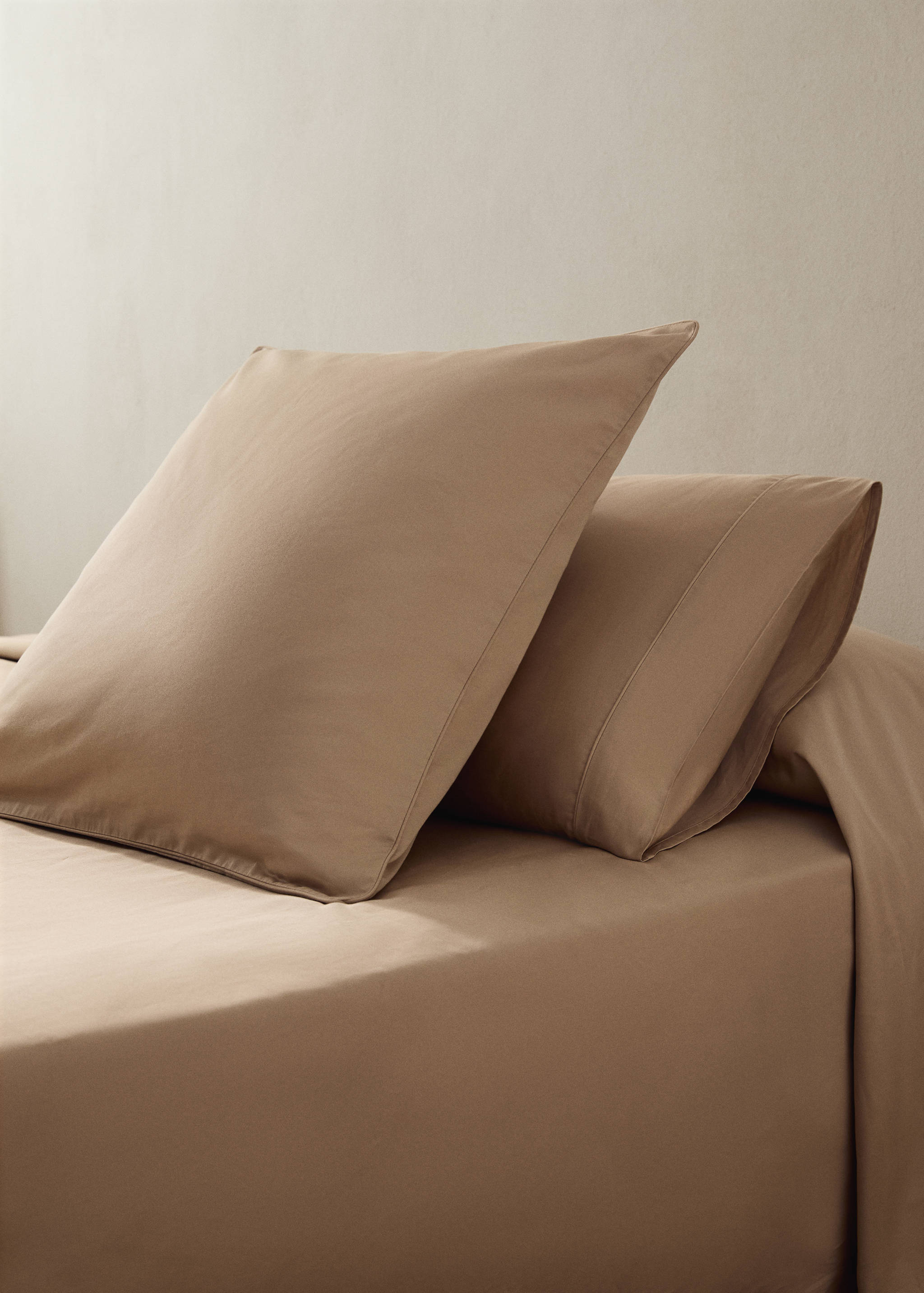 Taupe pillowcase on a made bed with matching linen.