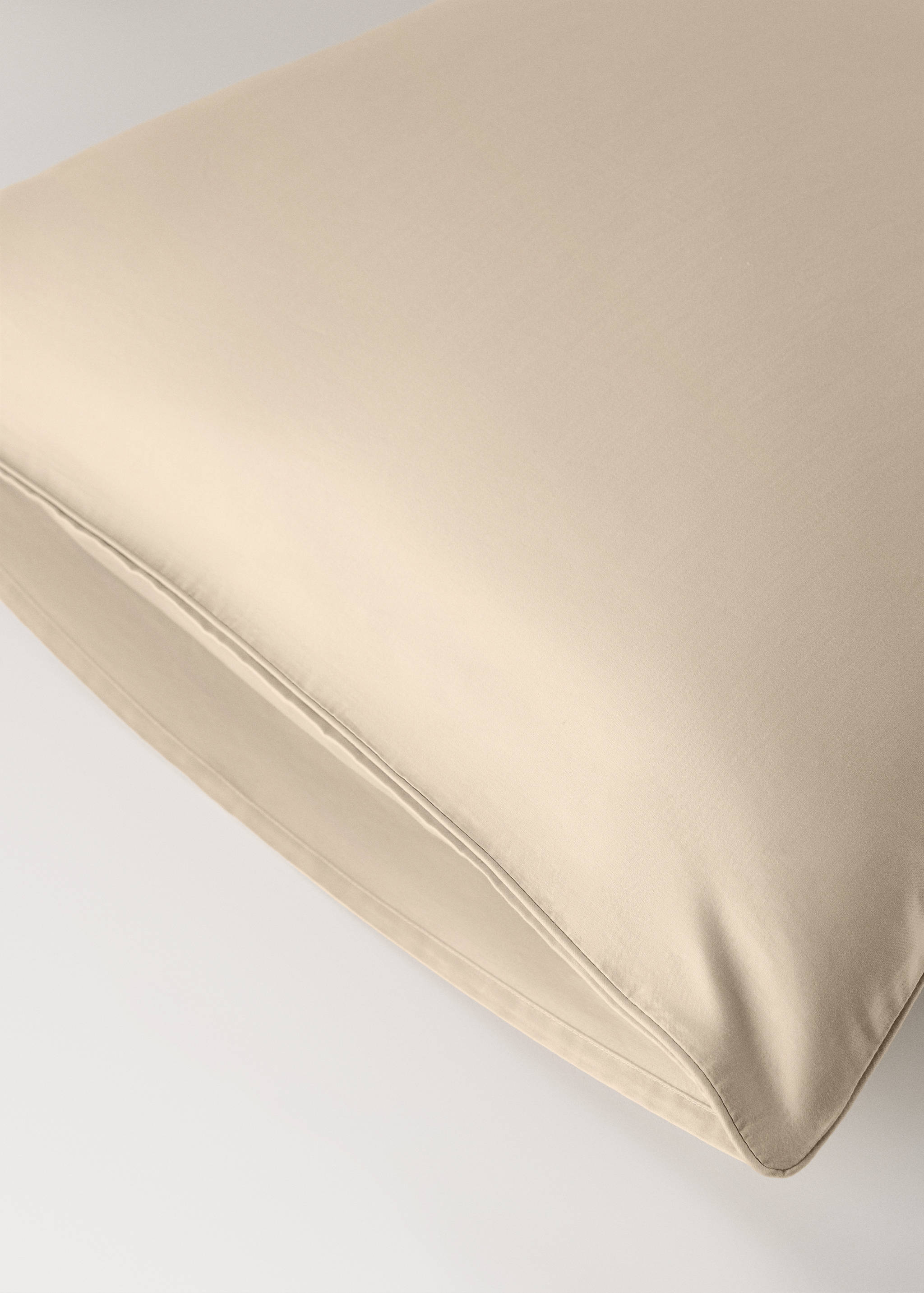 Beige pillowcase detail showing smooth fabric and piped edge.