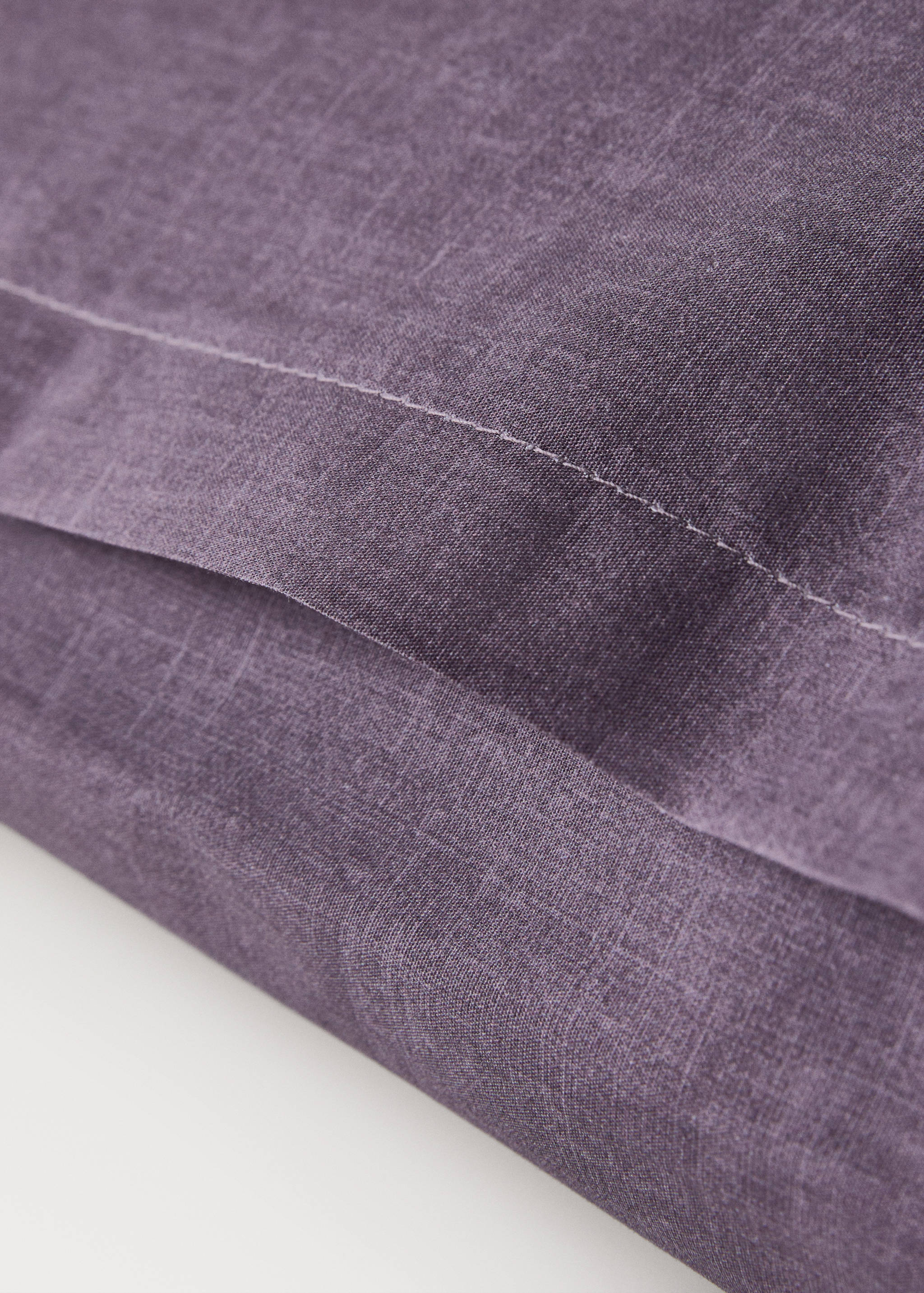 Purple pillowcase detail showing textured fabric and stitching.