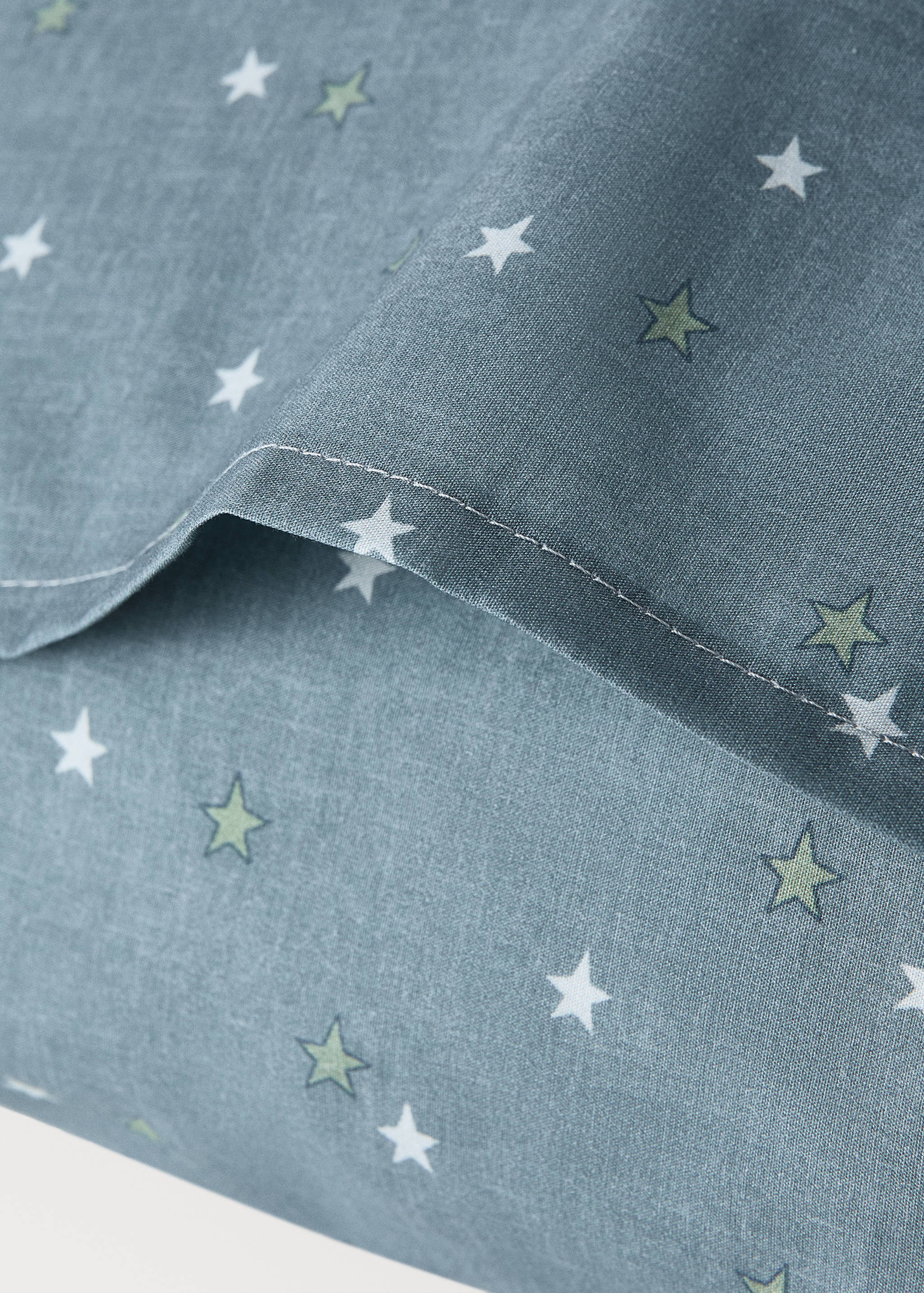 Greyish-blue star print pillowcase detail with white and green stars.