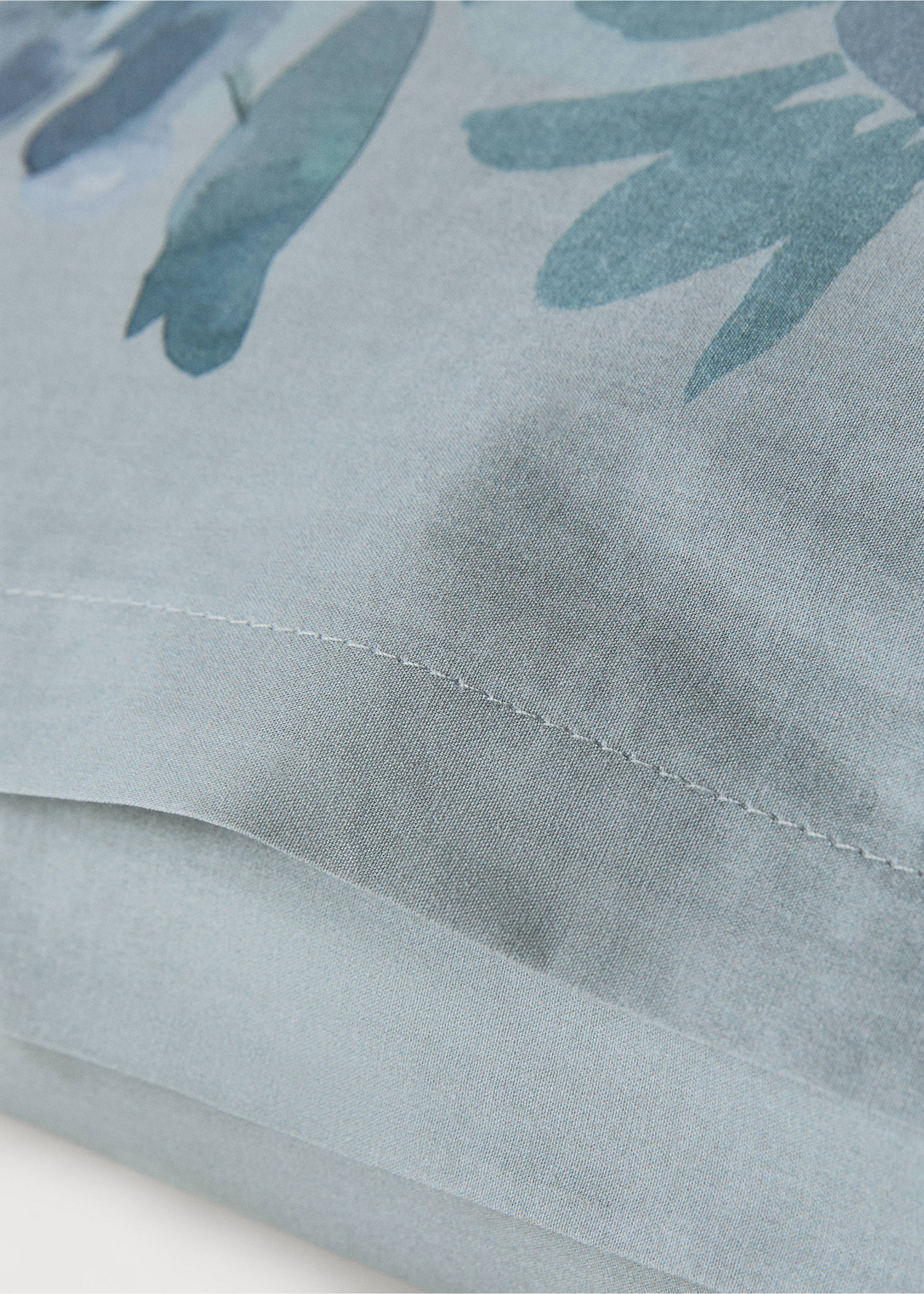 Blue pillowcase detail with a green floral pattern and stitched seam., Aqua Green. Ref: 17011628-00.