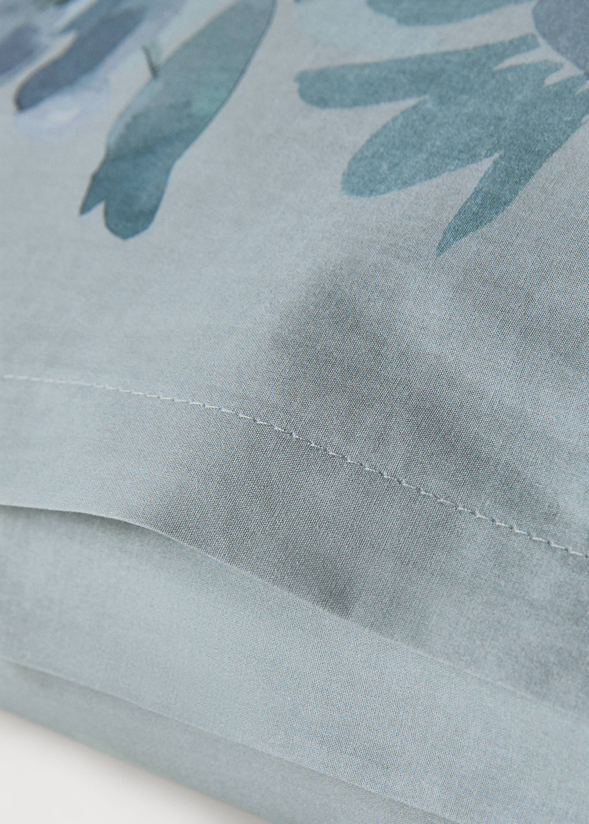 Blue pillowcase detail with a green floral pattern and stitched seam.