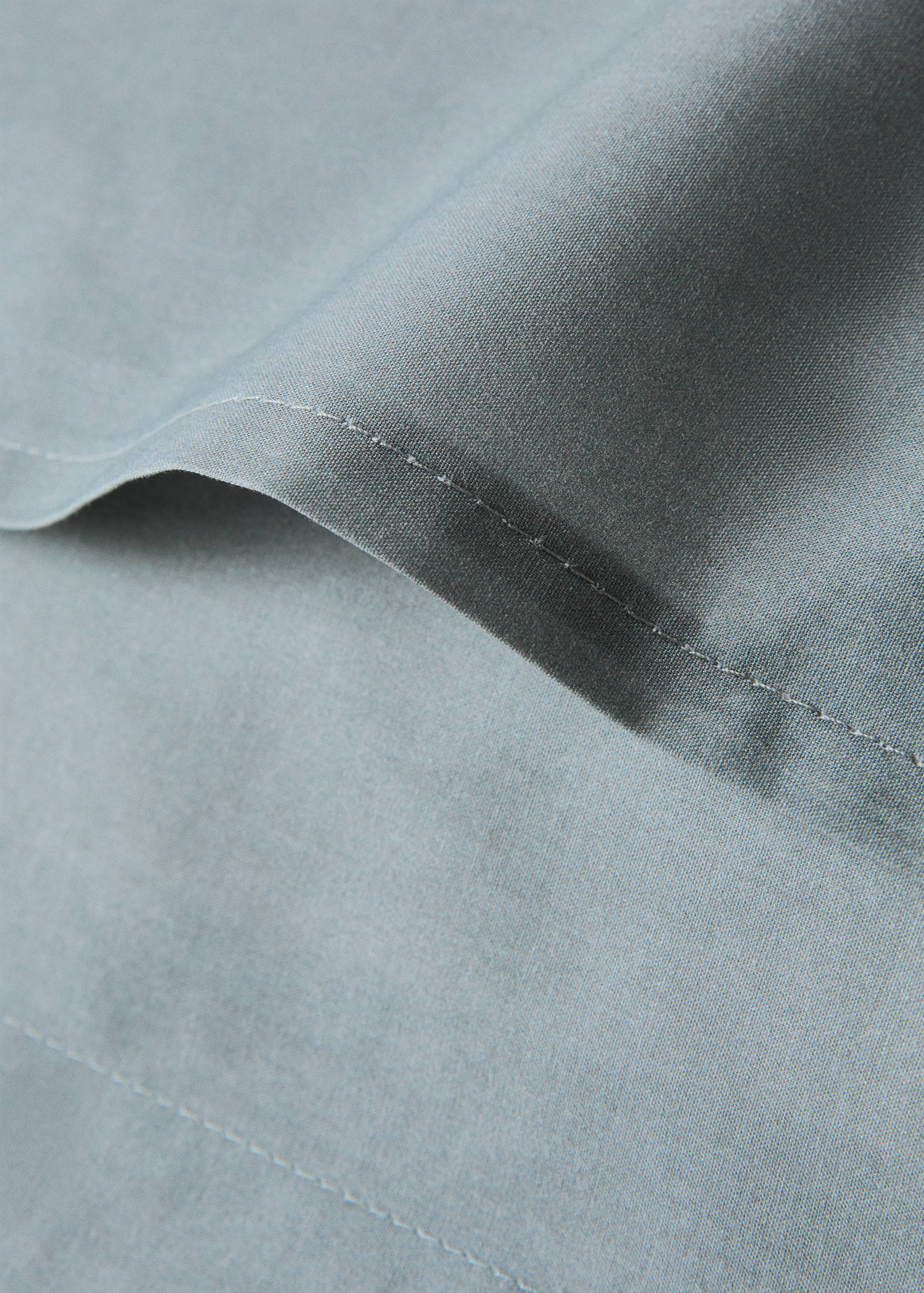 Close-up of a blue-grey pillowcase featuring fine texture and tonal stitching.