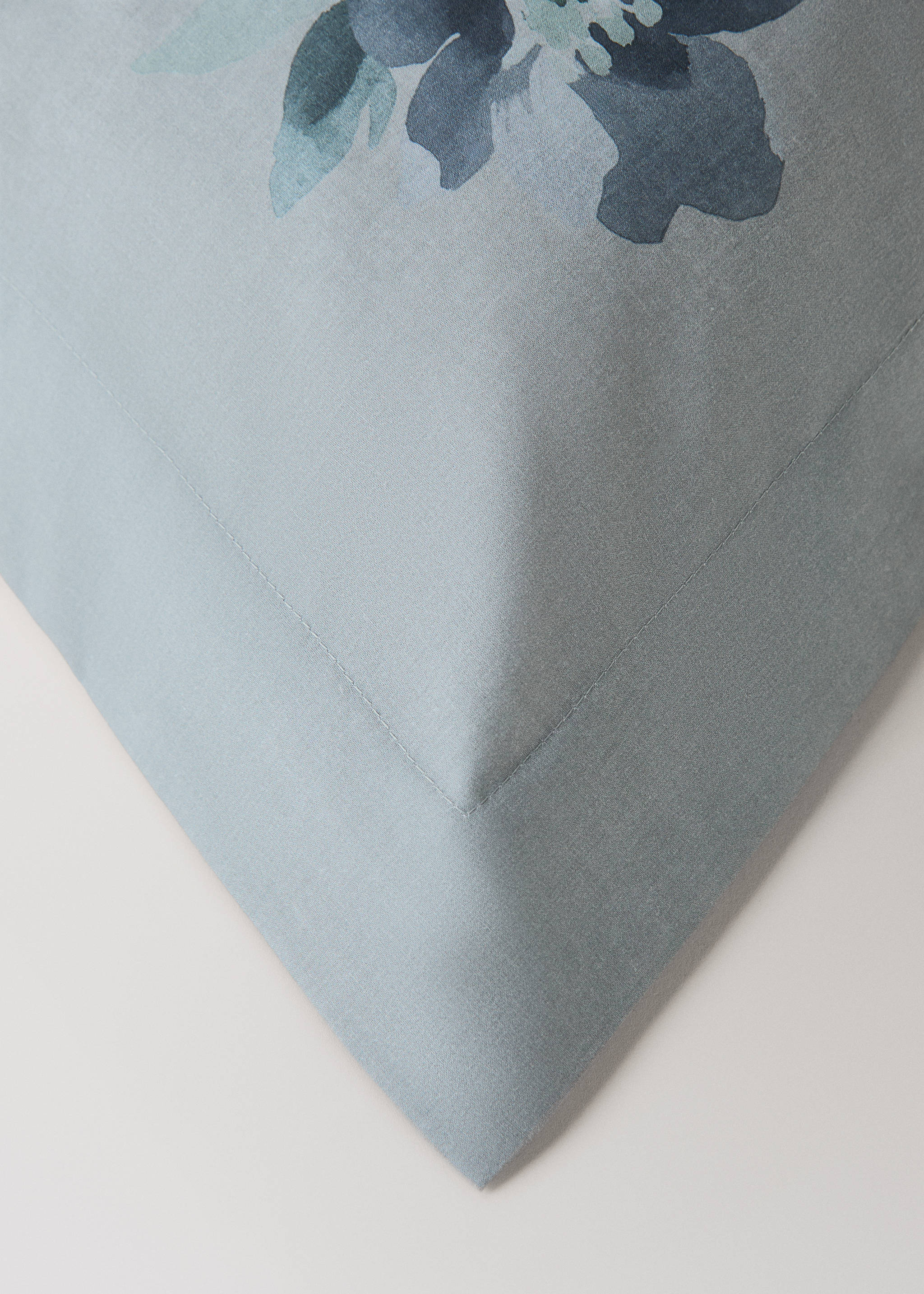 Close-up of a light blue pillowcase with a stitched flange and floral print detail.