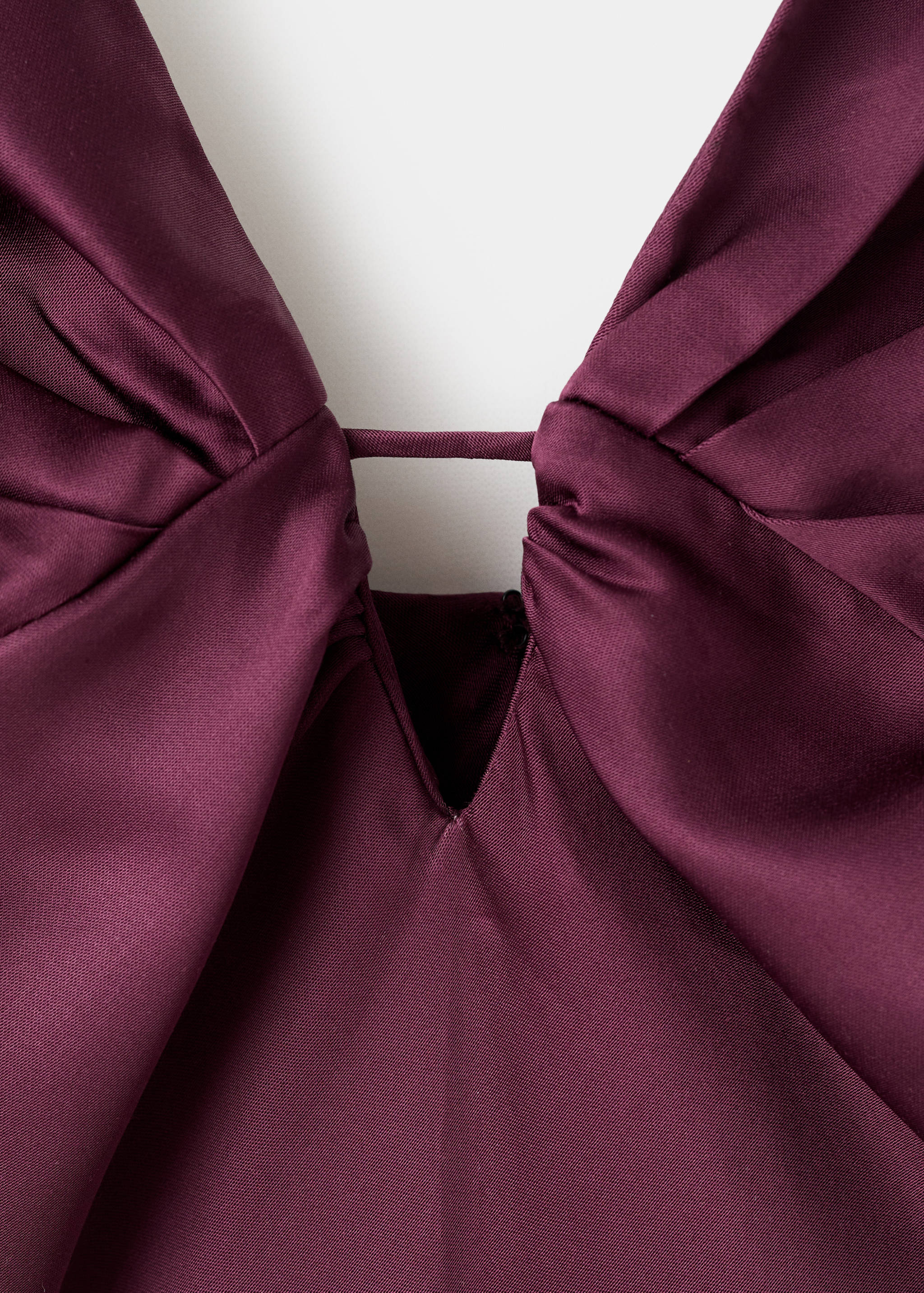 Burgundy dress bodice close-up, showing a pleated deep V-neckline with a fabric bridge detail.