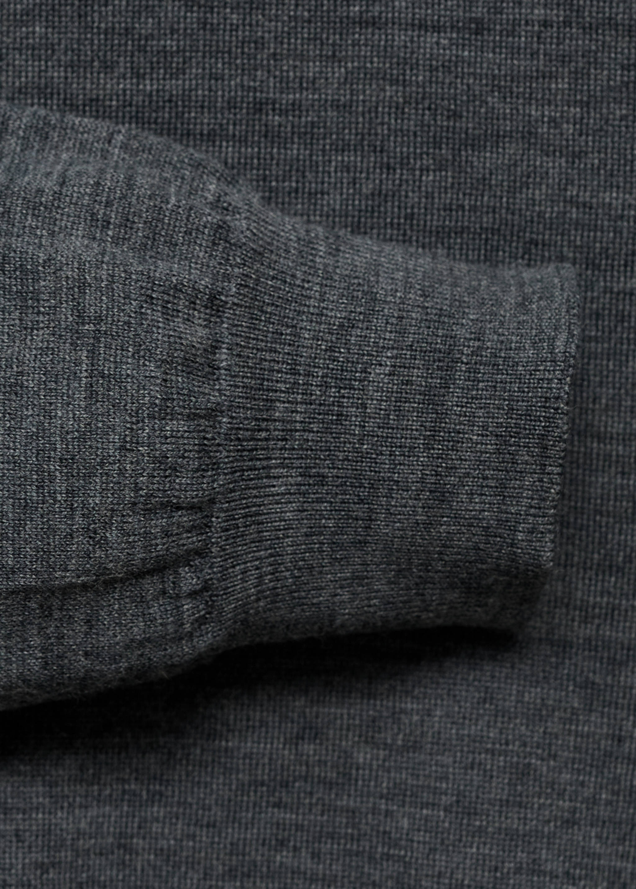 Close-up of the dark grey knitted fabric and ribbed cuff of a jersey.