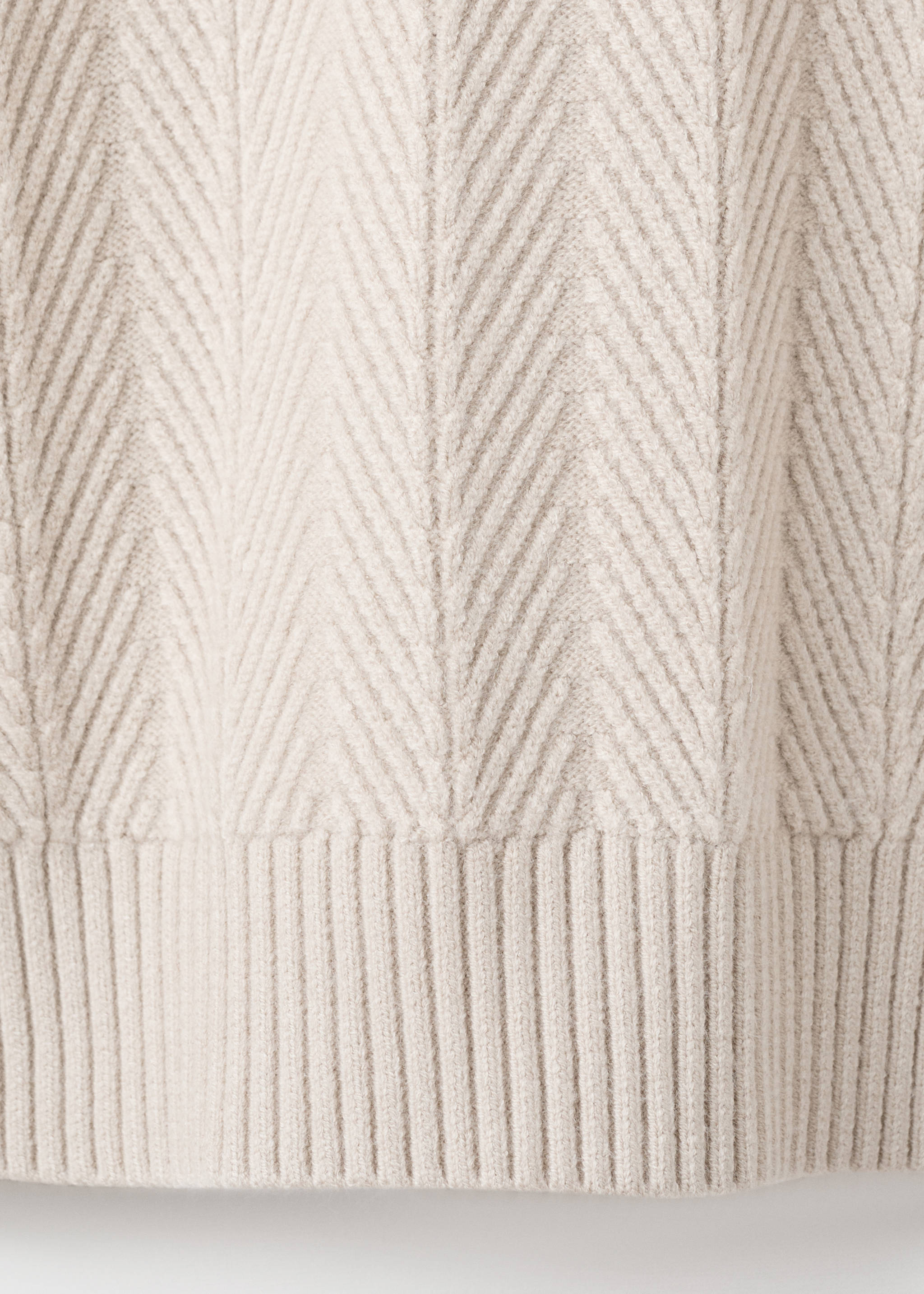 Close-up of a beige men's knit jumper with a chevron pattern and ribbed hem.