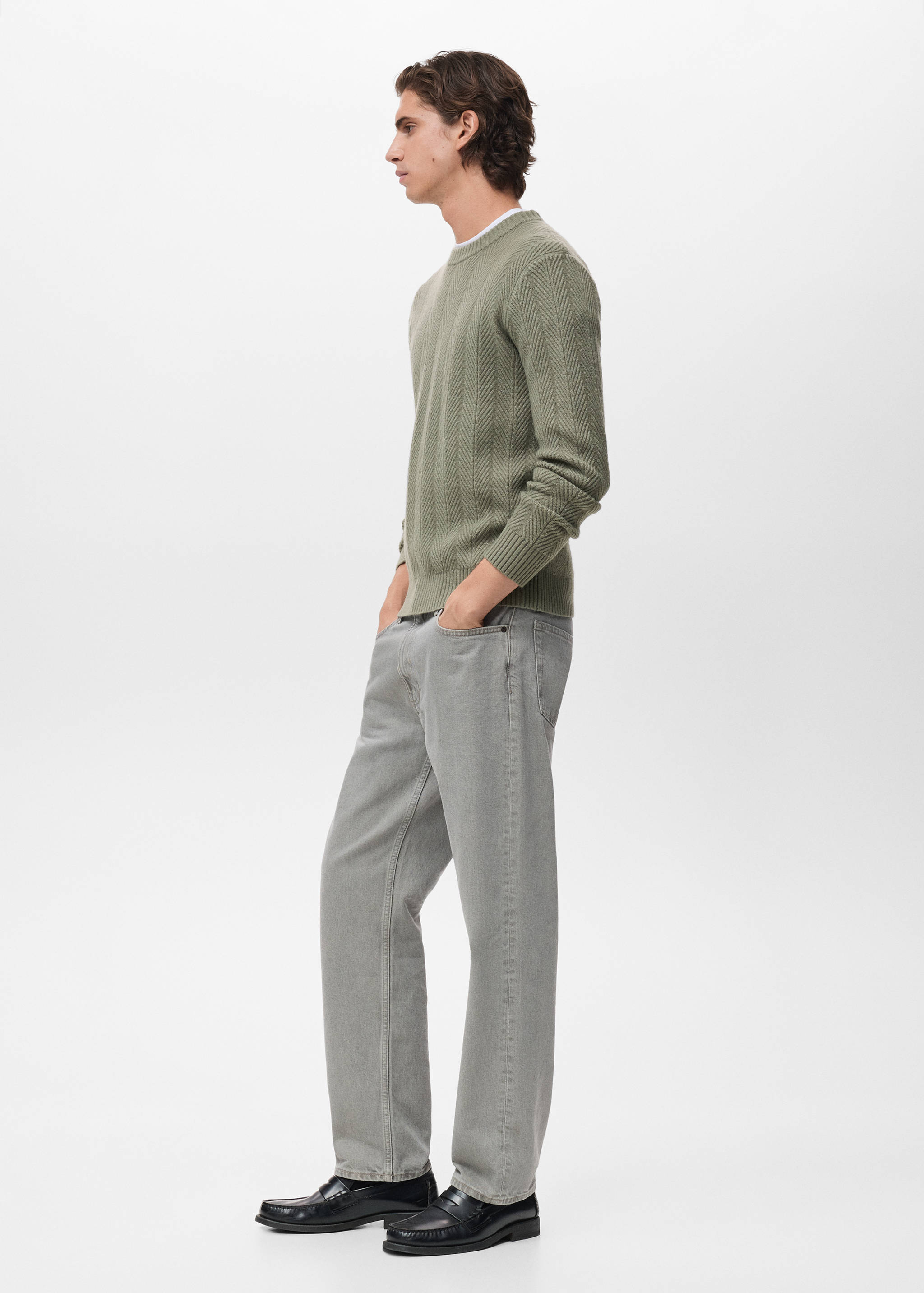 Sage green crew neck jersey in a knit pattern, worn with grey trousers.