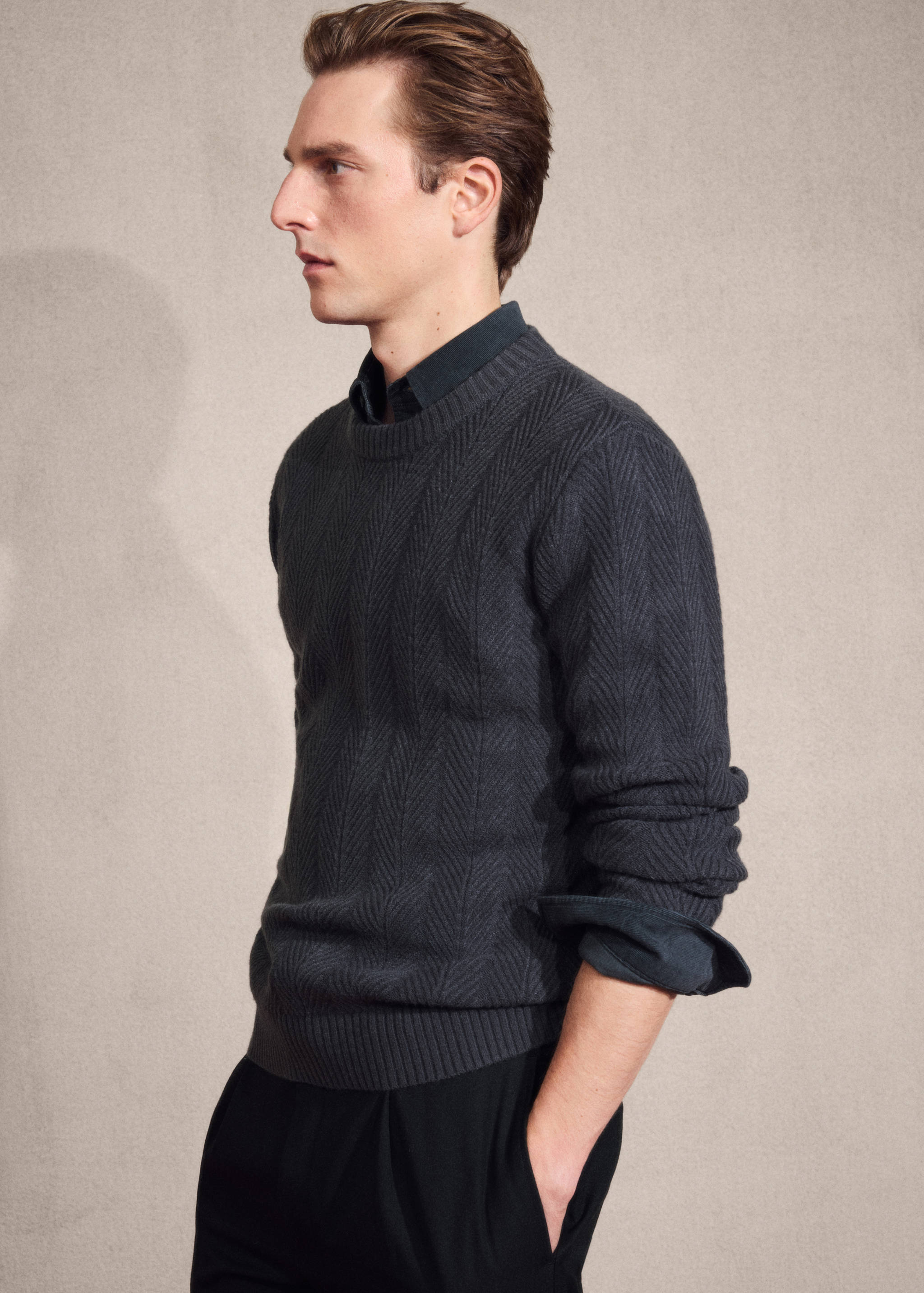 Dark grey crew-neck jumper in a knitted chevron pattern, worn over a dark shirt.