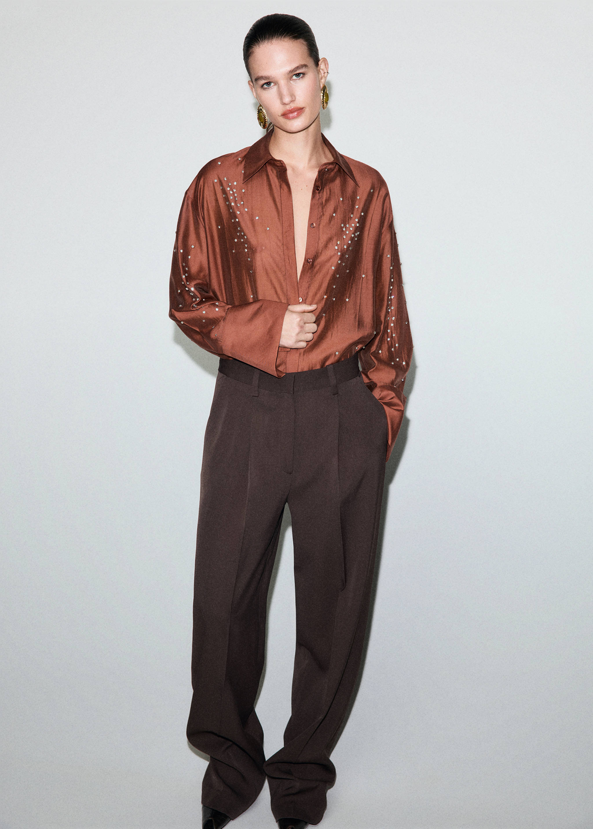 Brown satin shirt with rhinestone embellishments, worn with brown trousers.