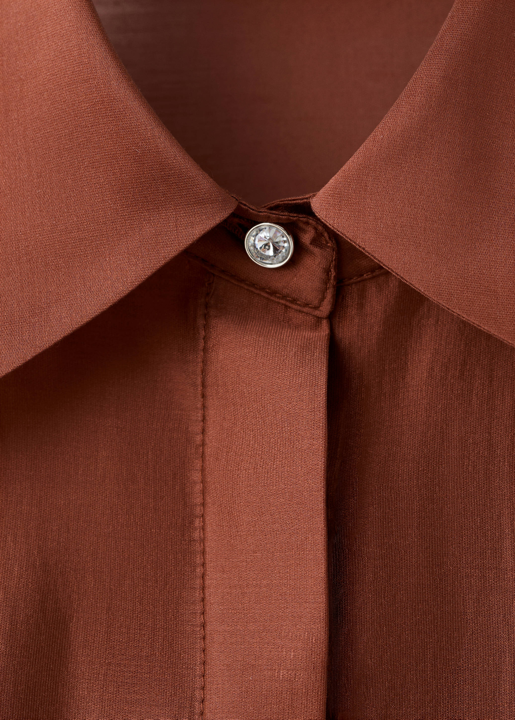 Close-up of a terracotta brown shirt collar with a single crystal top button.