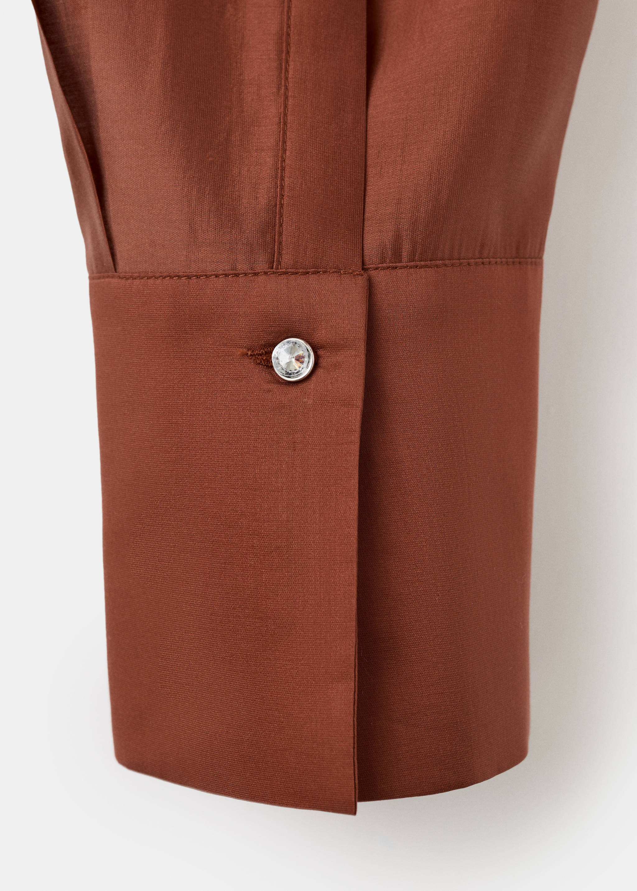 Close-up of a rust brown shirt cuff with a crystal button.