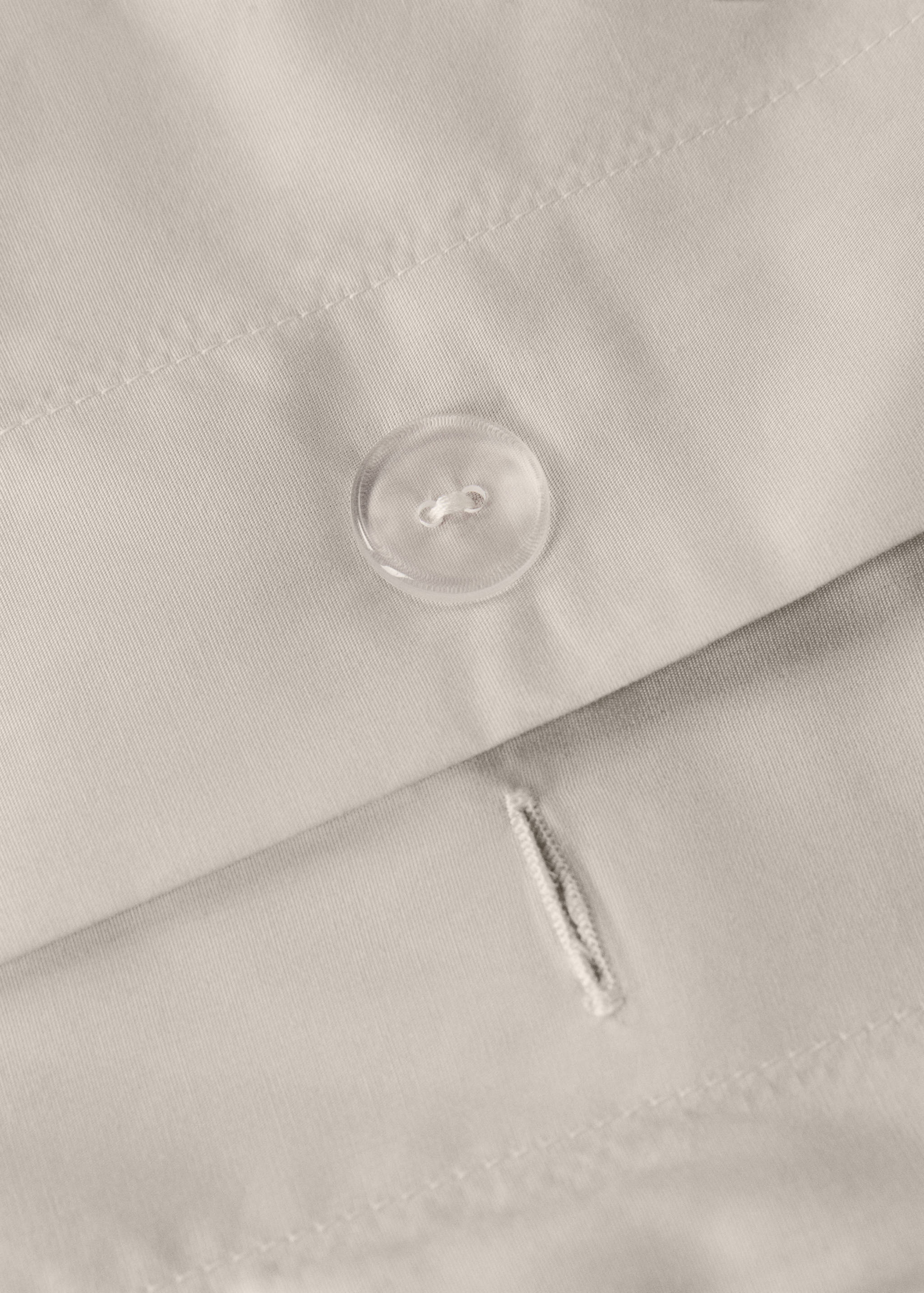 Close-up of a light beige duvet cover showing button closure detail.