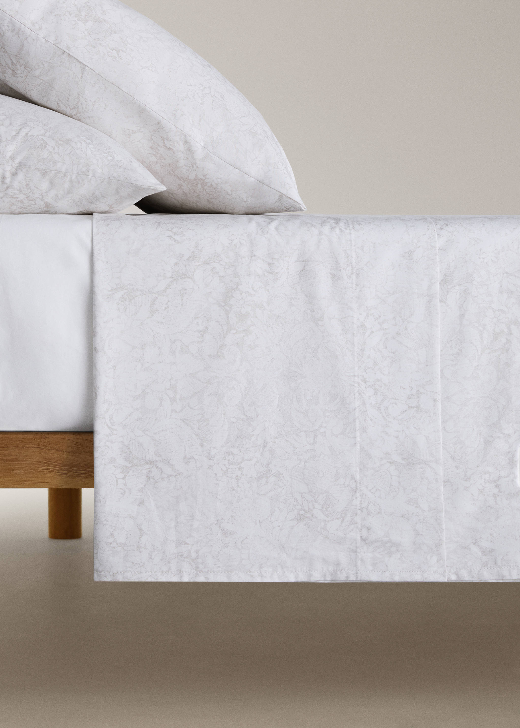 White flat sheet with a subtle grey botanical print on a made bed.