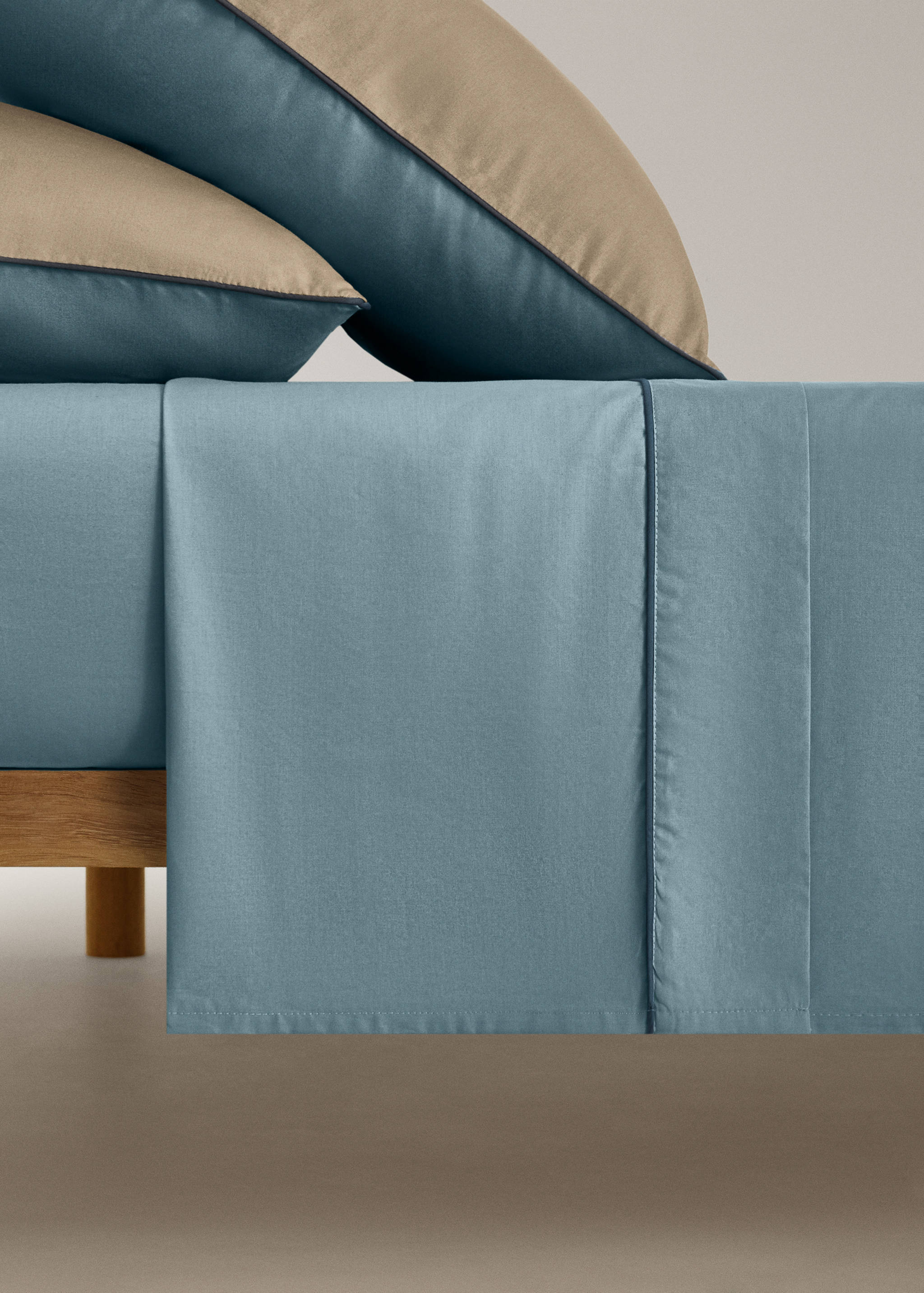 Blue flat sheet with a dark blue piped trim on a made bed.
