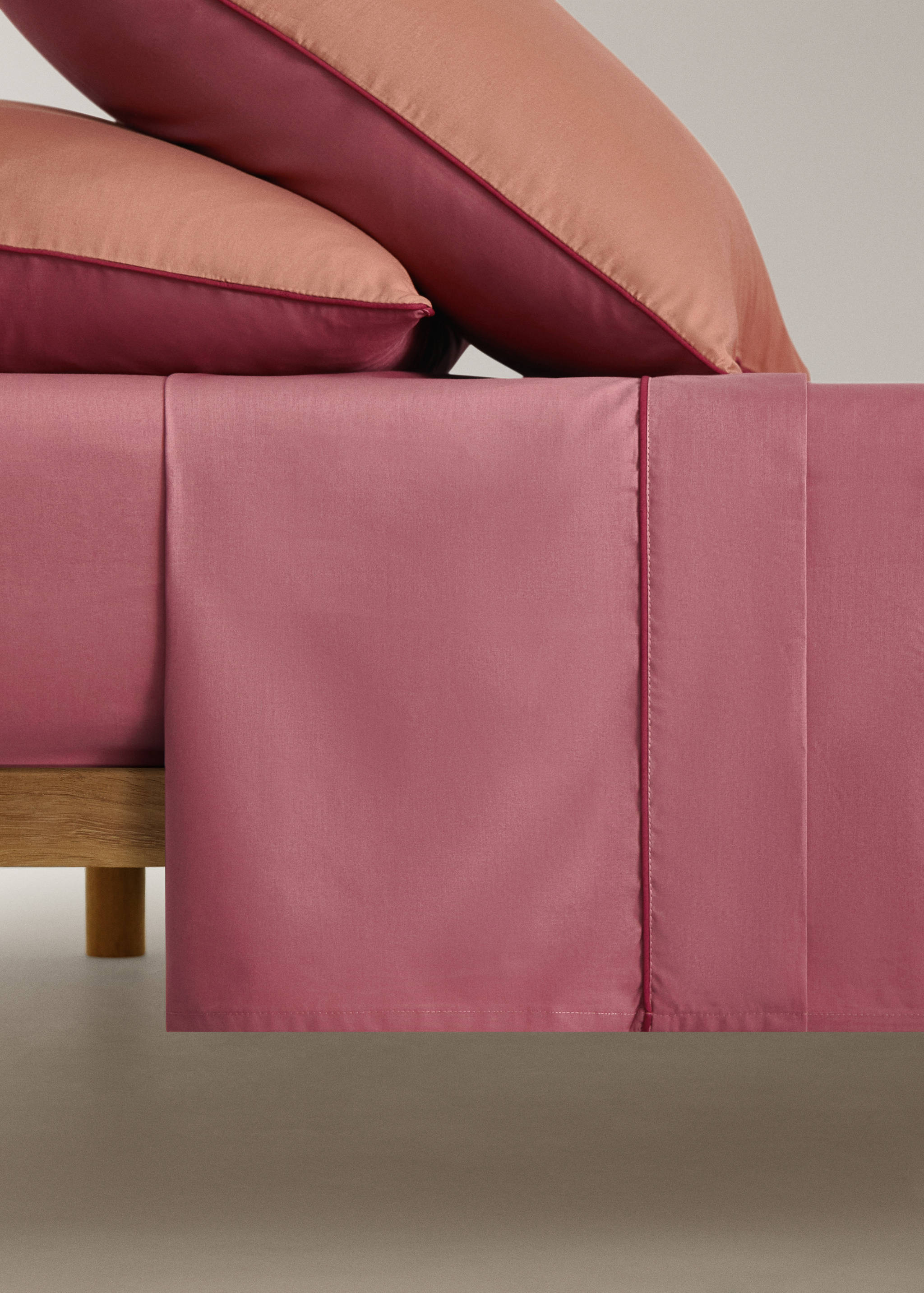Mauve pink flat sheet with contrasting maroon piped trim on a bed.