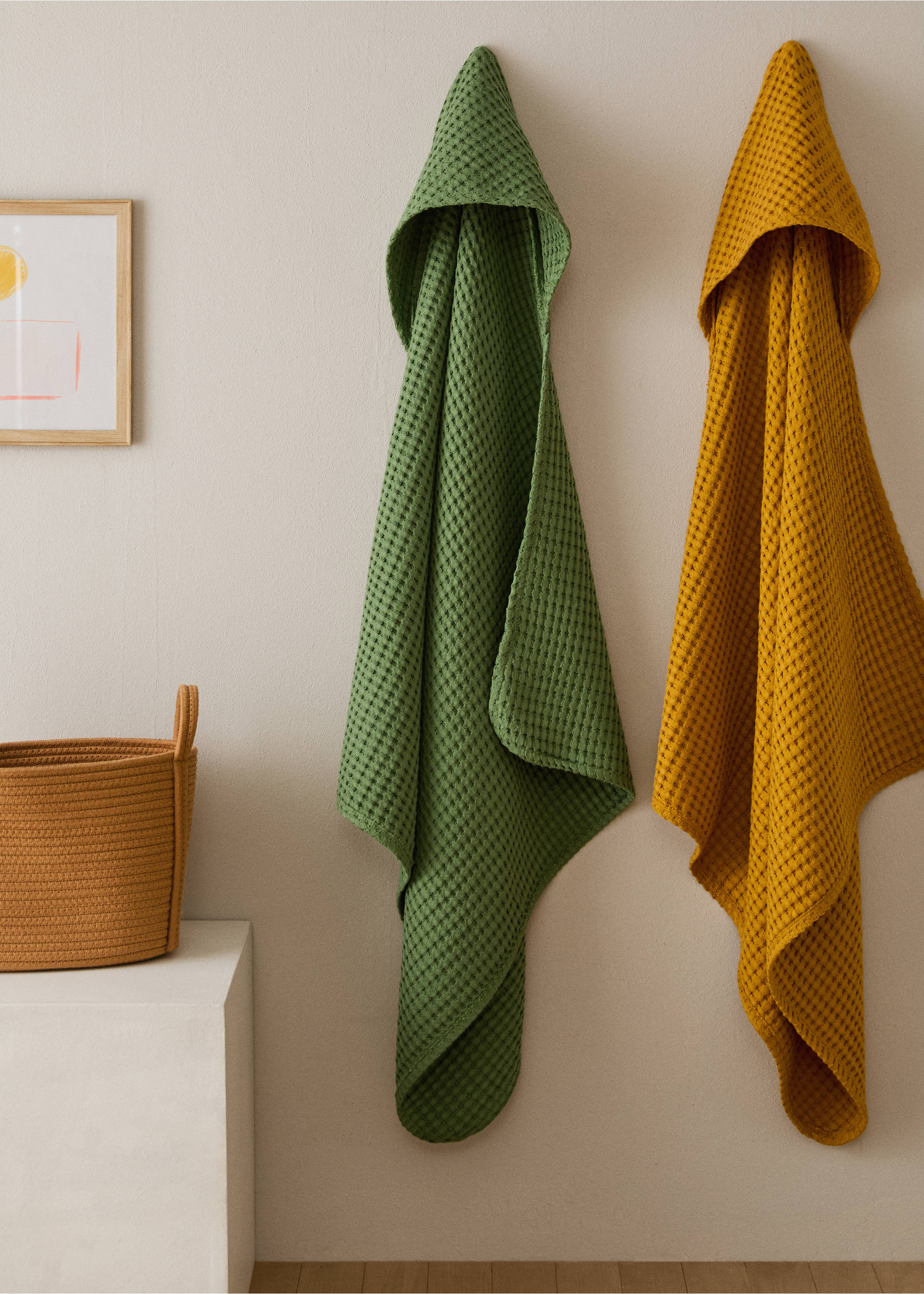 Green and mustard yellow hooded waffle-weave towels hanging on a wall., Green. Ref: 17021627-00.