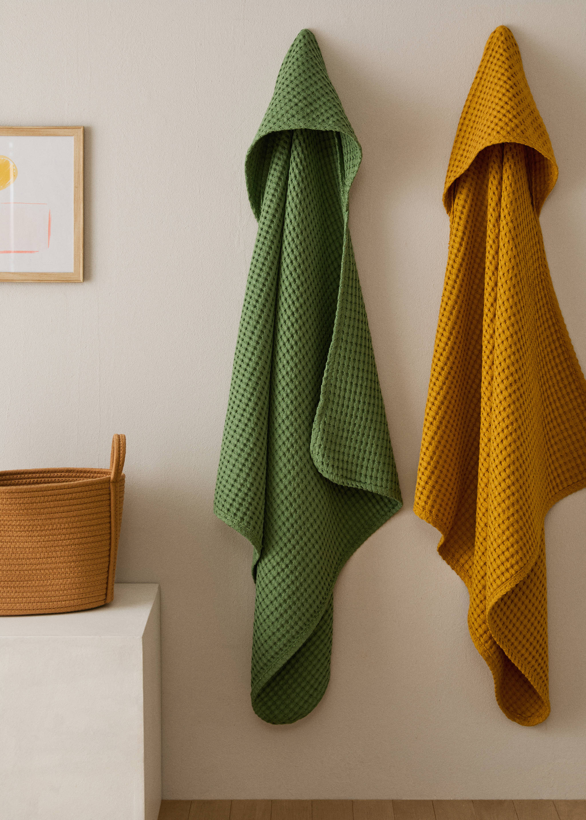 Green and mustard yellow hooded waffle-weave towels hanging on a wall.
