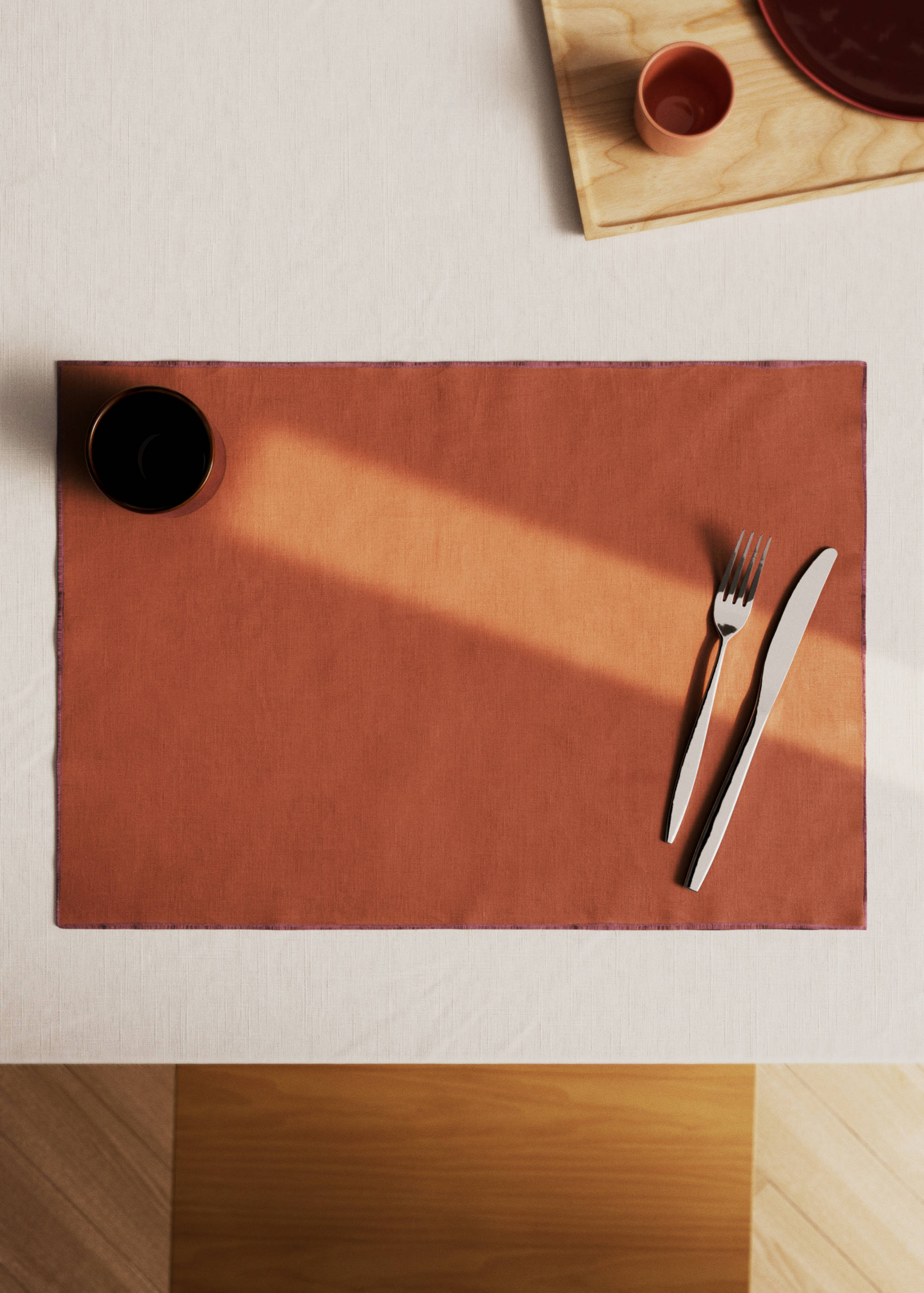 Rectangular terracotta placemat styled with tableware on a light tablecloth.