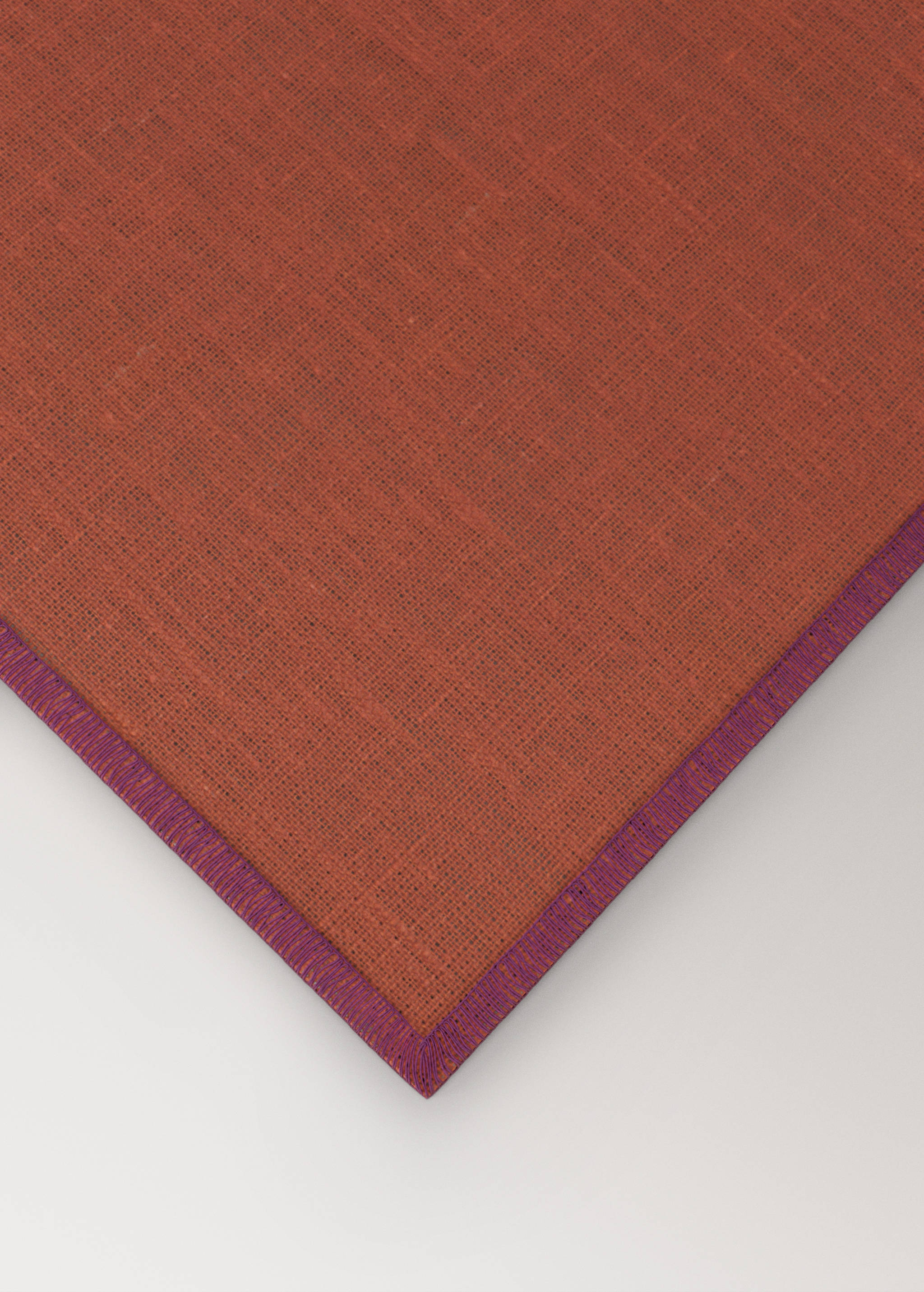 Rust-orange placemat with a woven texture and contrasting purple embroidered border.