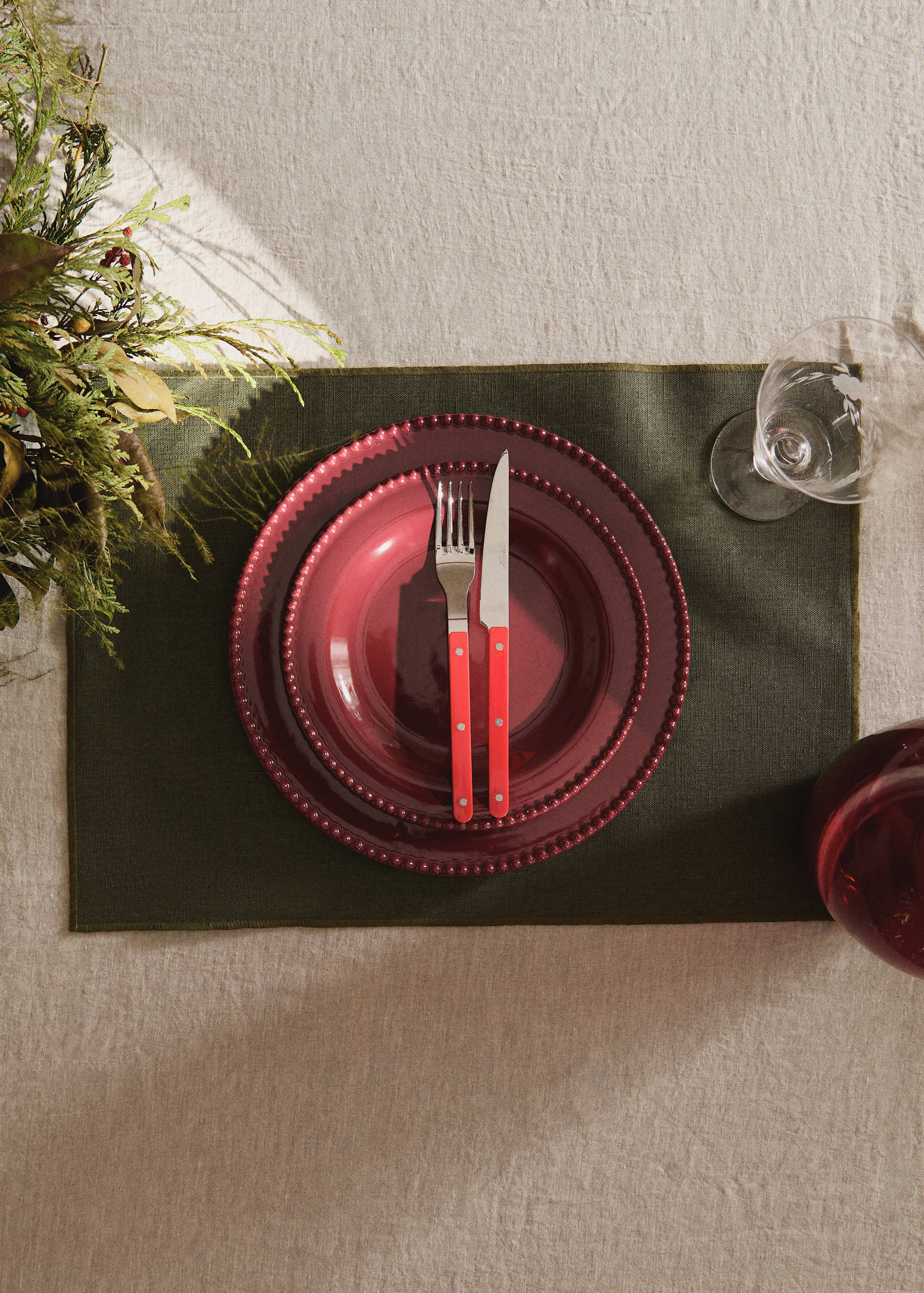 Dark green rectangular textile placemat styled with red plates and cutlery.