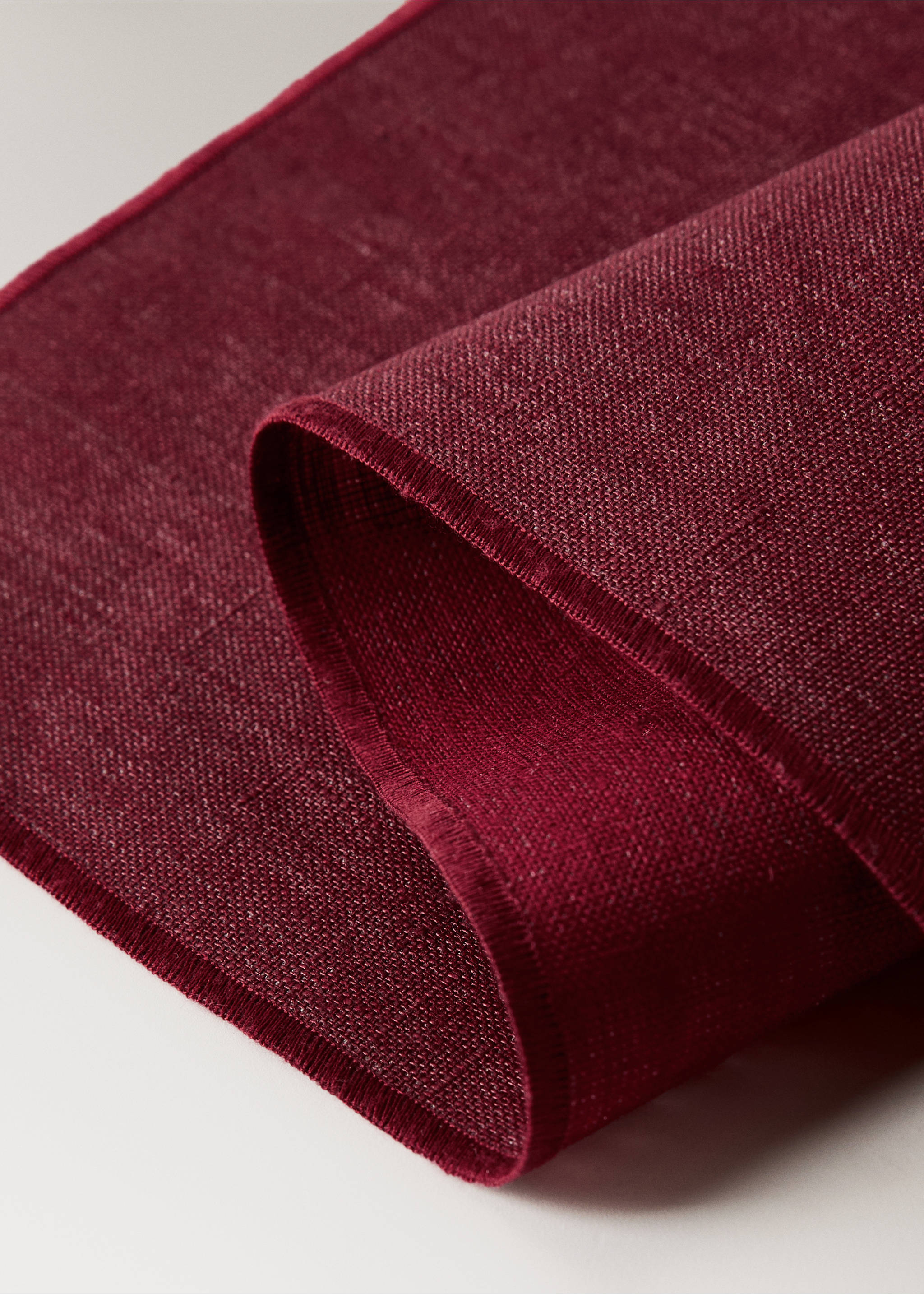Burgundy textured placemat with a stitched border shown in close-up., Red. Ref: 17024133-00.