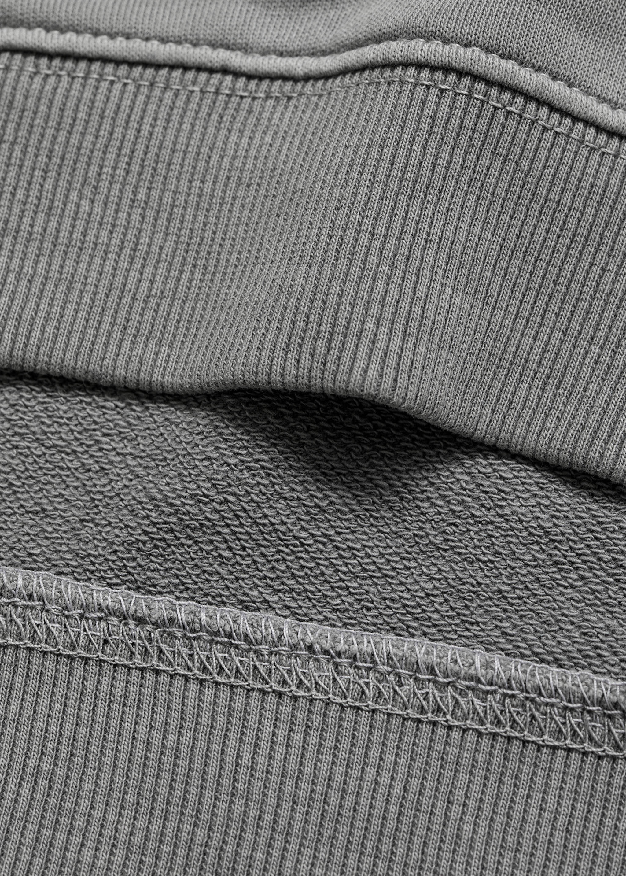 Close-up of grey sweatshirt fabric showing the ribbed hem and interior fleece texture.