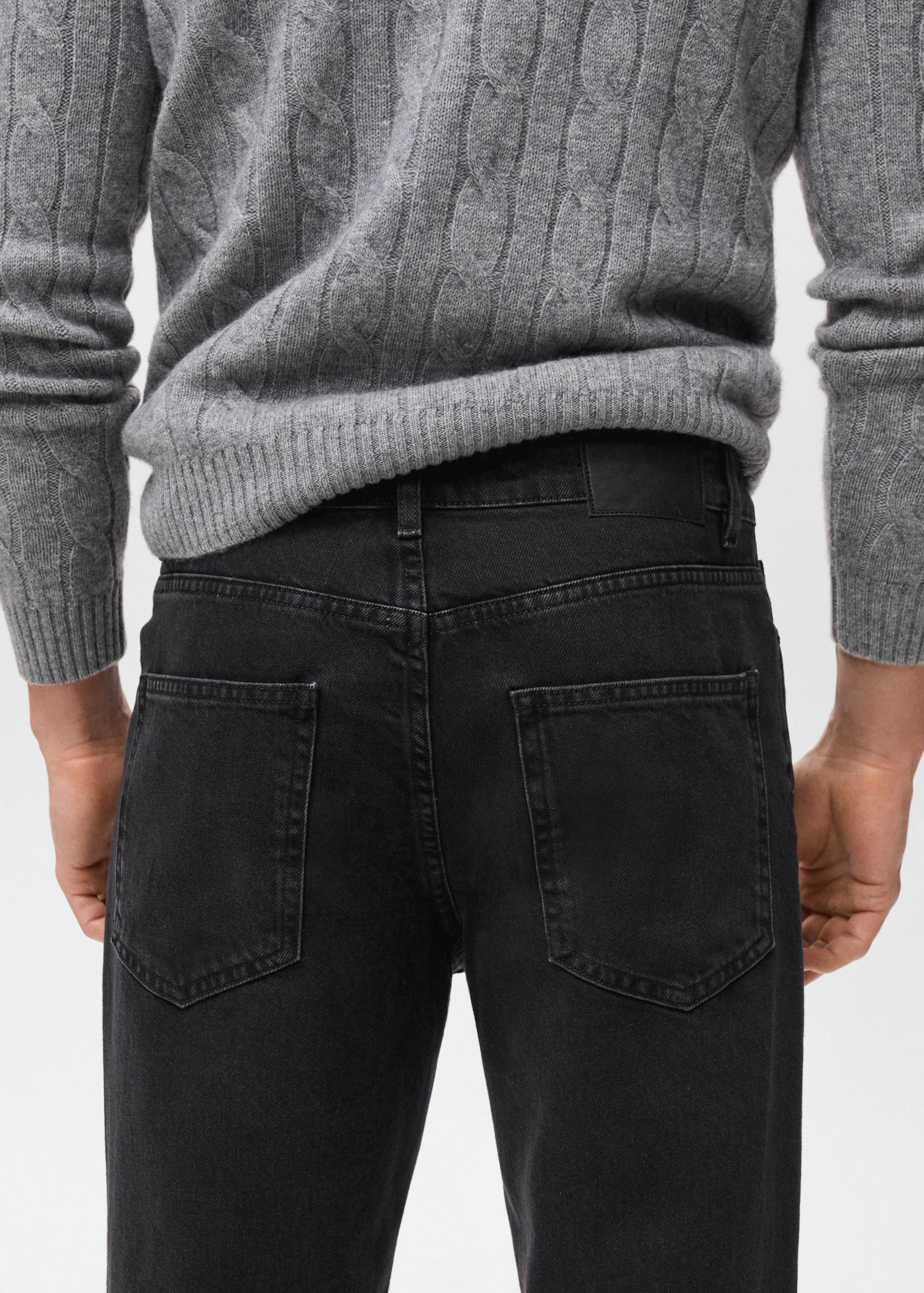 Black denim jeans shown from the back, paired with a grey jumper.