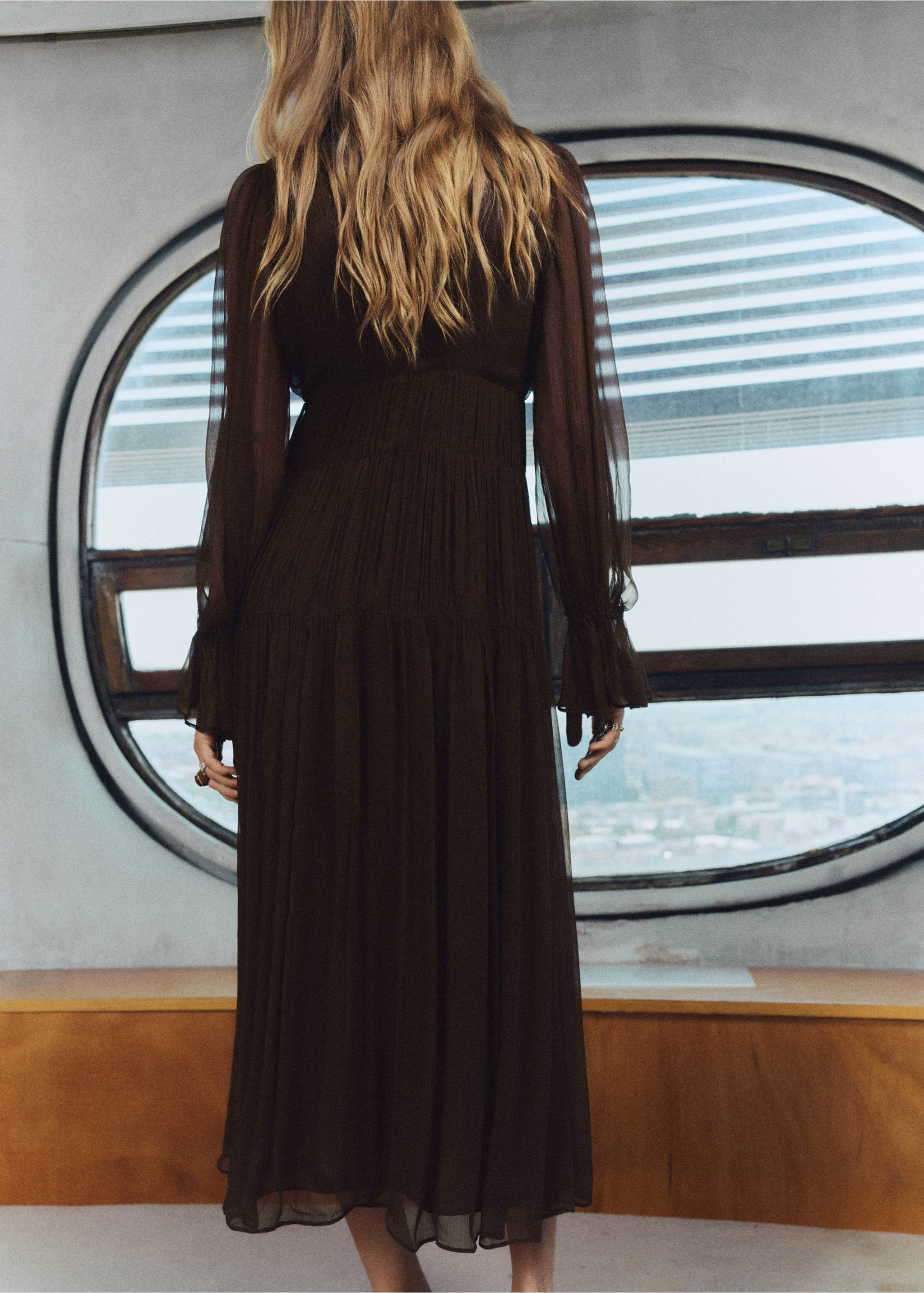Back view of a dark brown midi dress with long sheer sleeves and a tiered pleated skirt., Chocolate. Ref: 17025815-00.