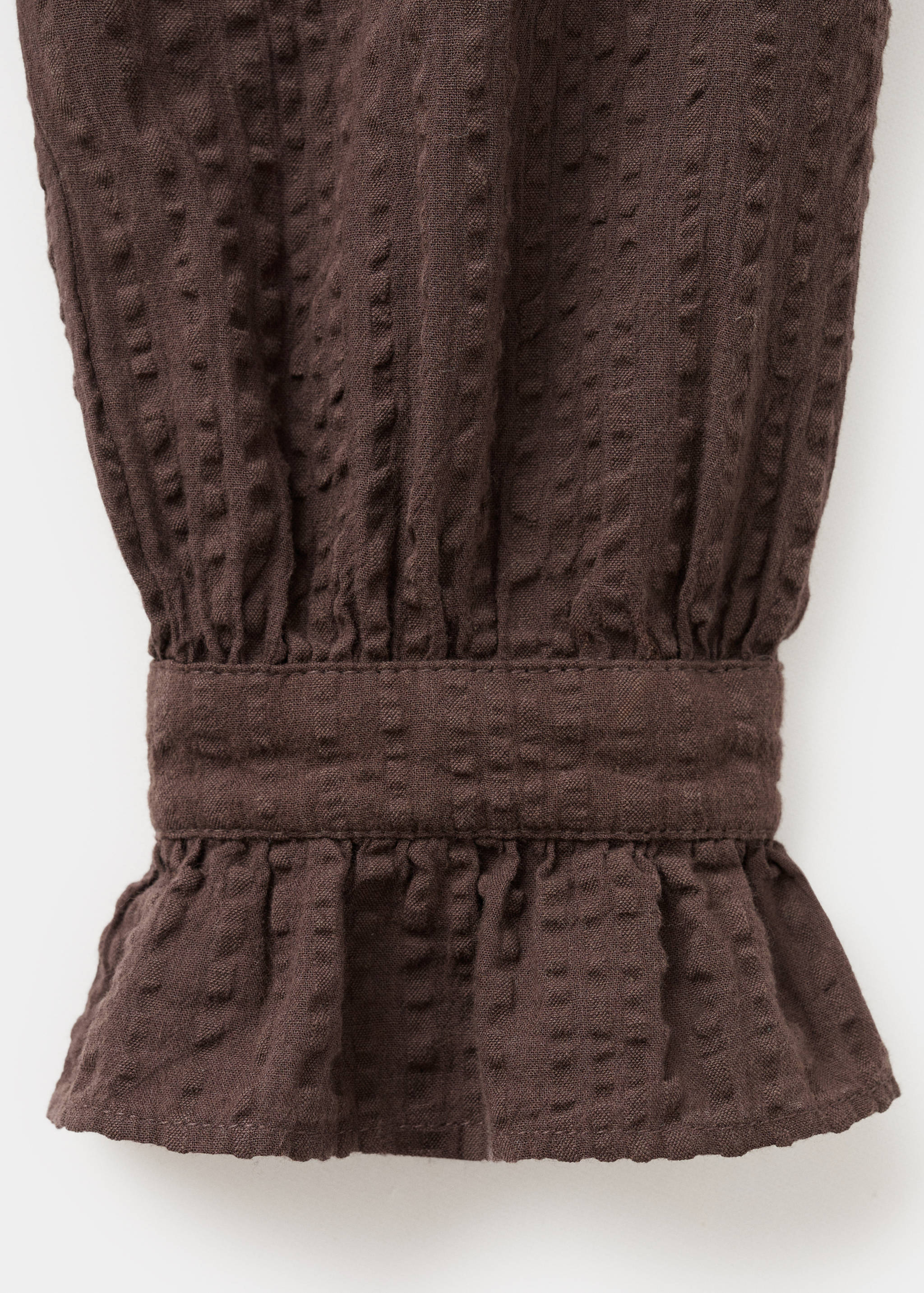 Brown textured blouse cuff detail with smocking and a ruffled hem.