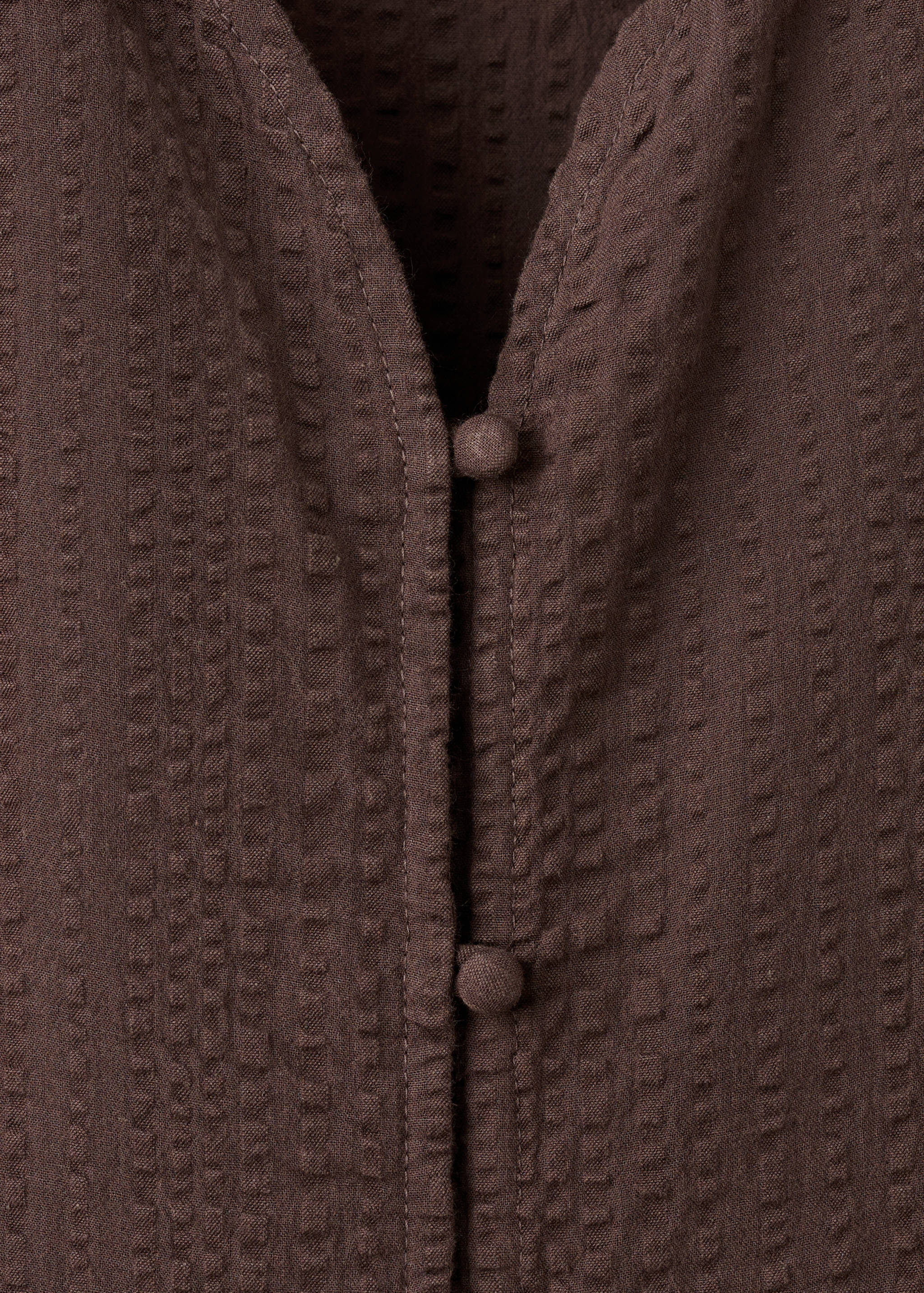 Brown textured blouse fabric close-up showing button details.