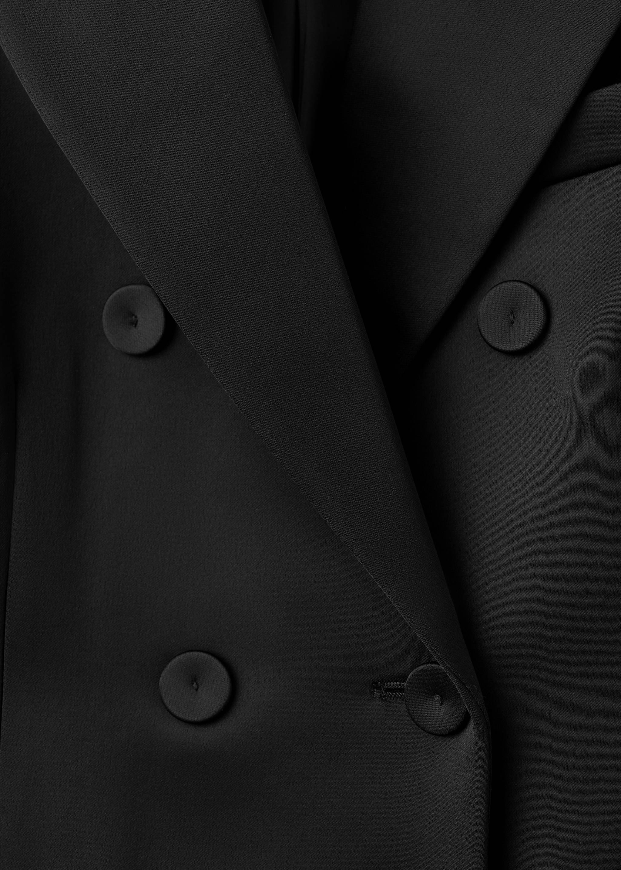 Close-up of the black blazer fabric and button detail.