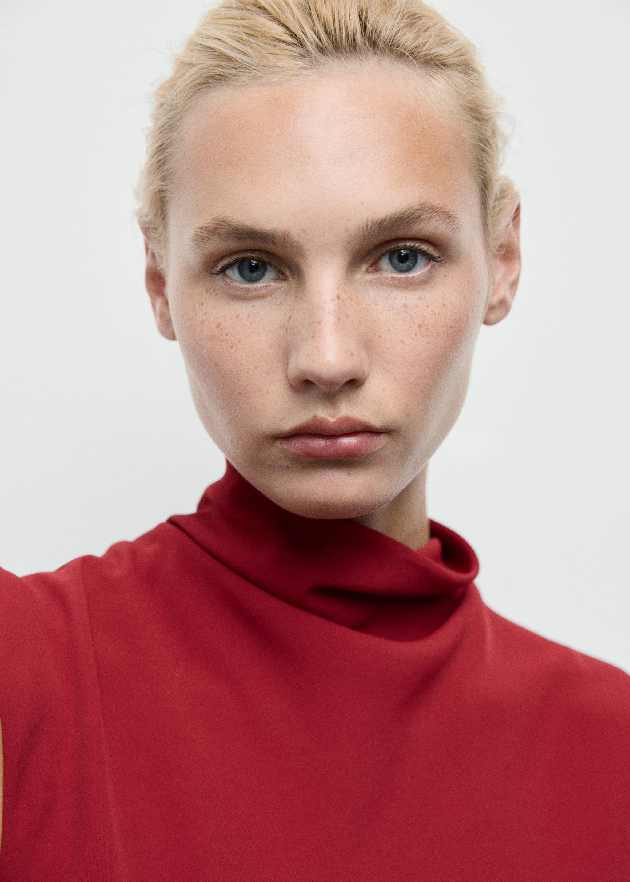 Close-up of a model wearing a red dress with a high draped neckline.