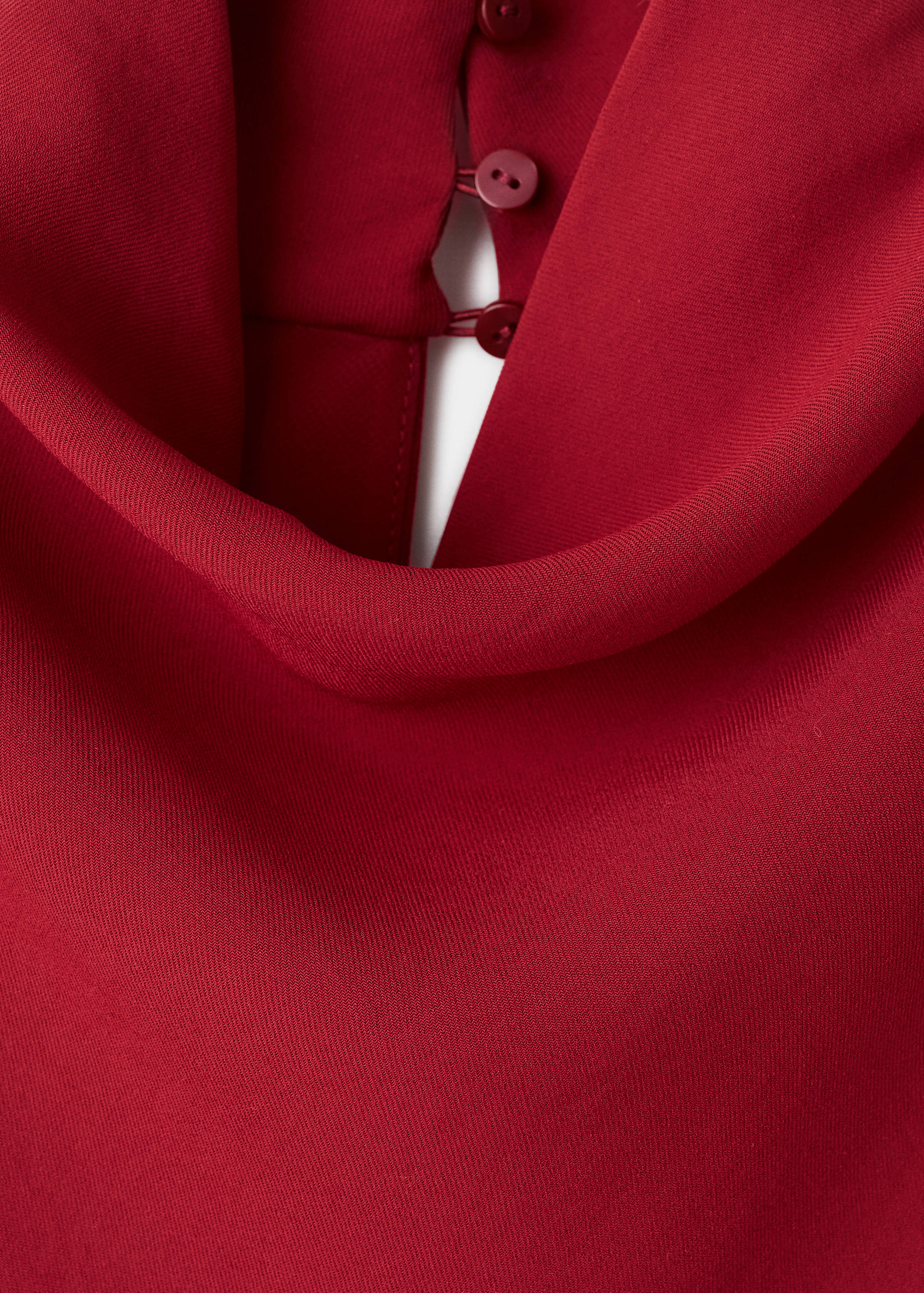 Close-up of the red dress showing the back cowl neckline and button detail.