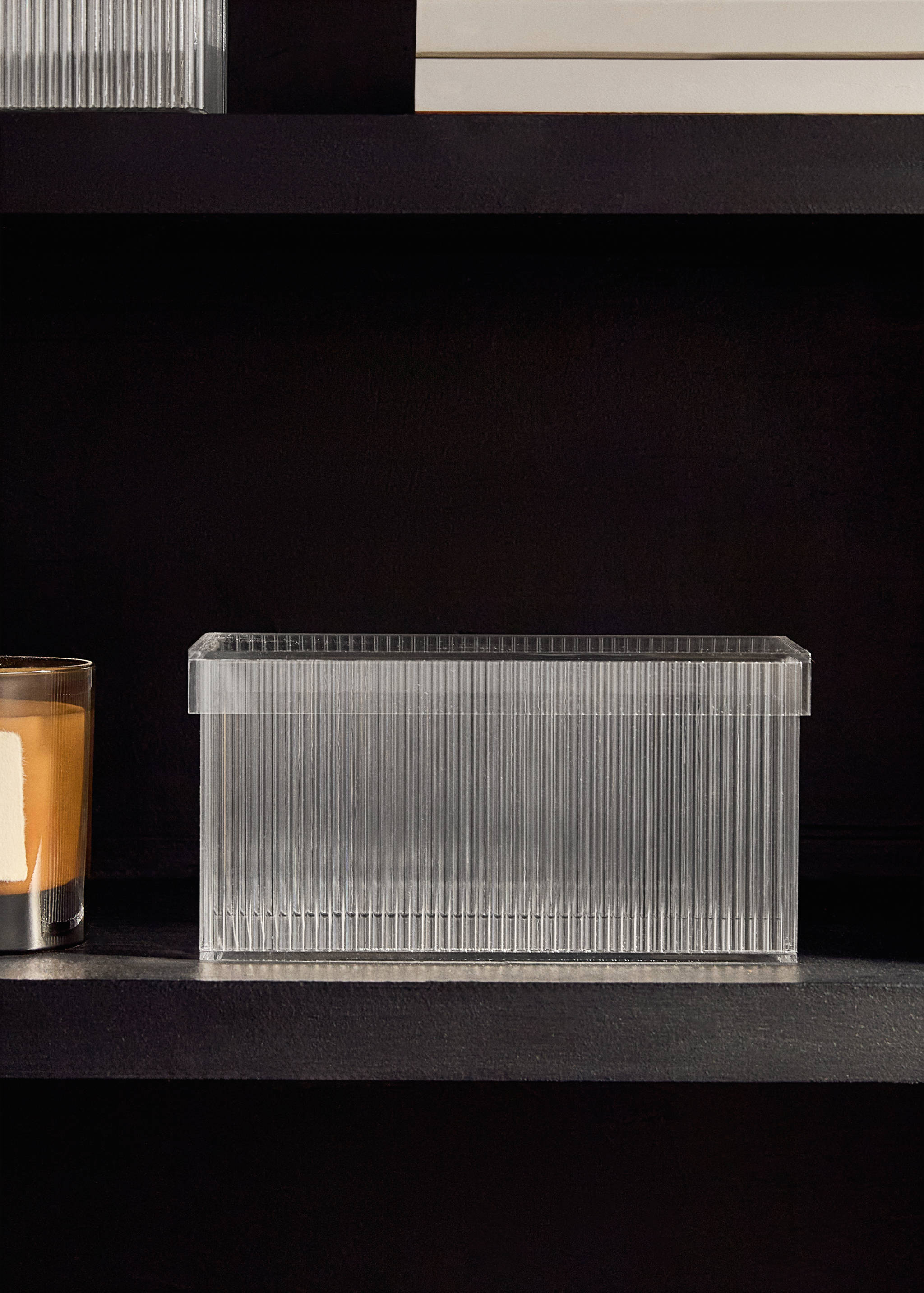 Clear fluted storage box with lid on a dark shelf.