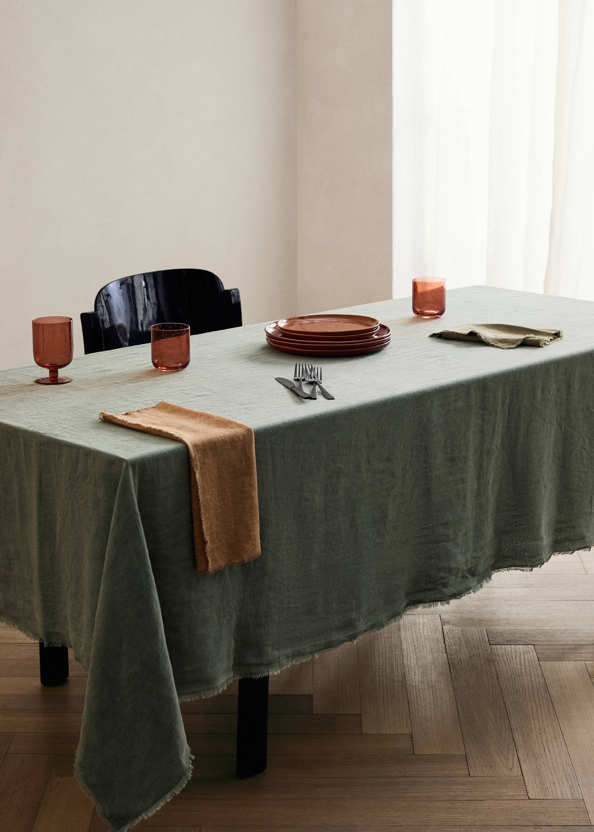 Sage green linen tablecloth with frayed edges on a set dining table.