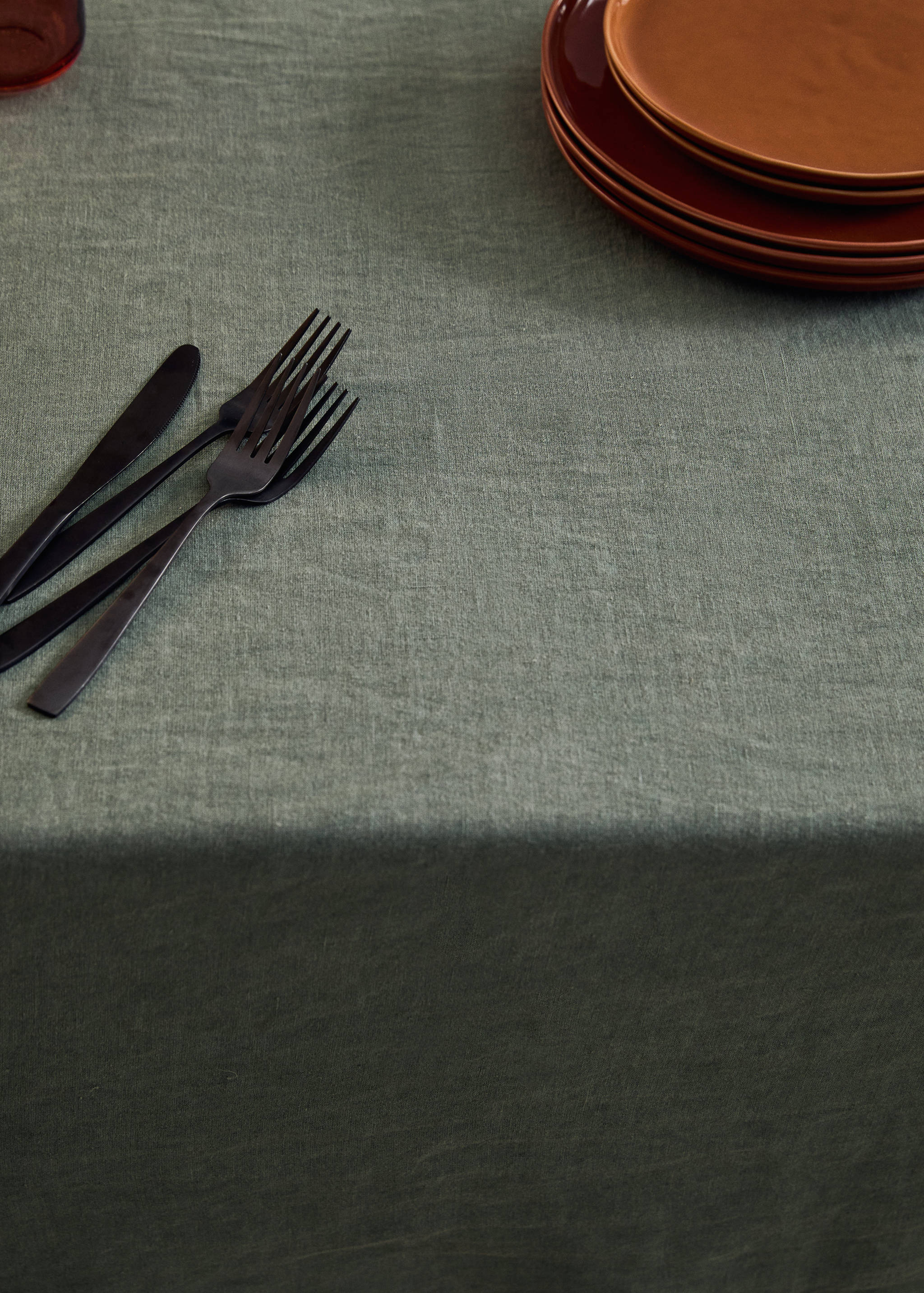 Green tablecloth set with dark cutlery and rust-orange plates.