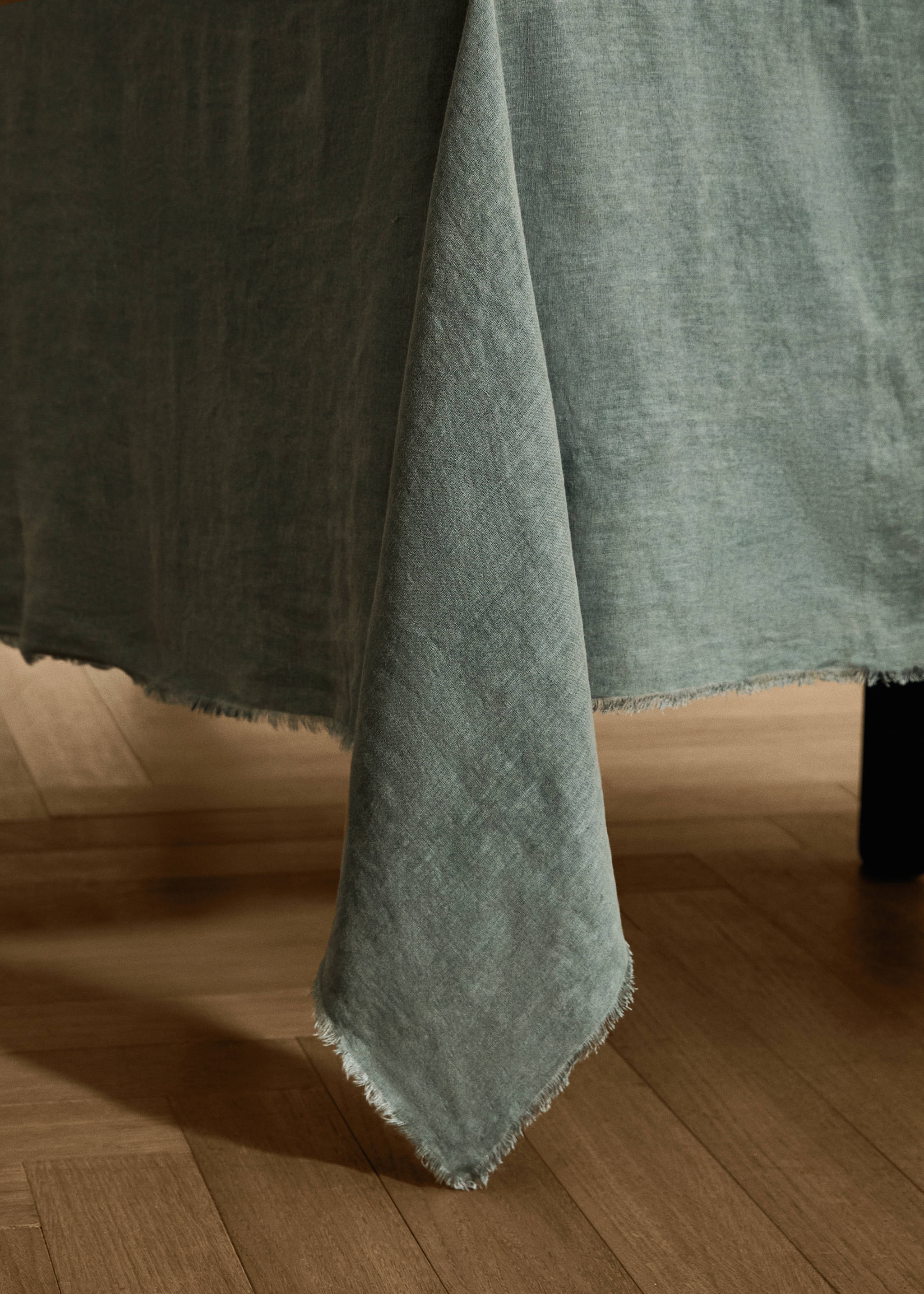 Green textured tablecloth with frayed edges draped over a table.