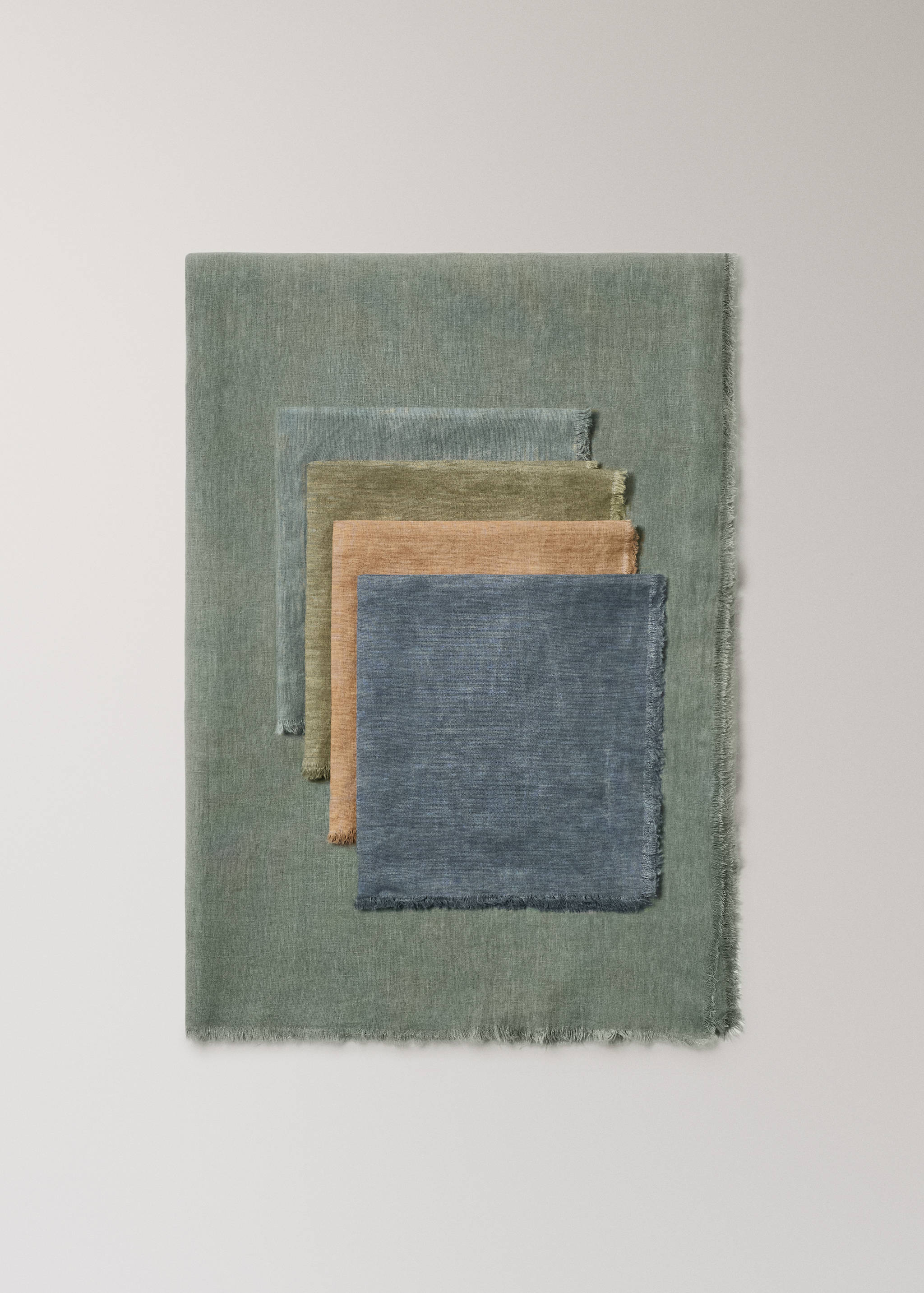 Sage green tablecloth featuring frayed edges with a stacked assortment of multi-coloured napkins.