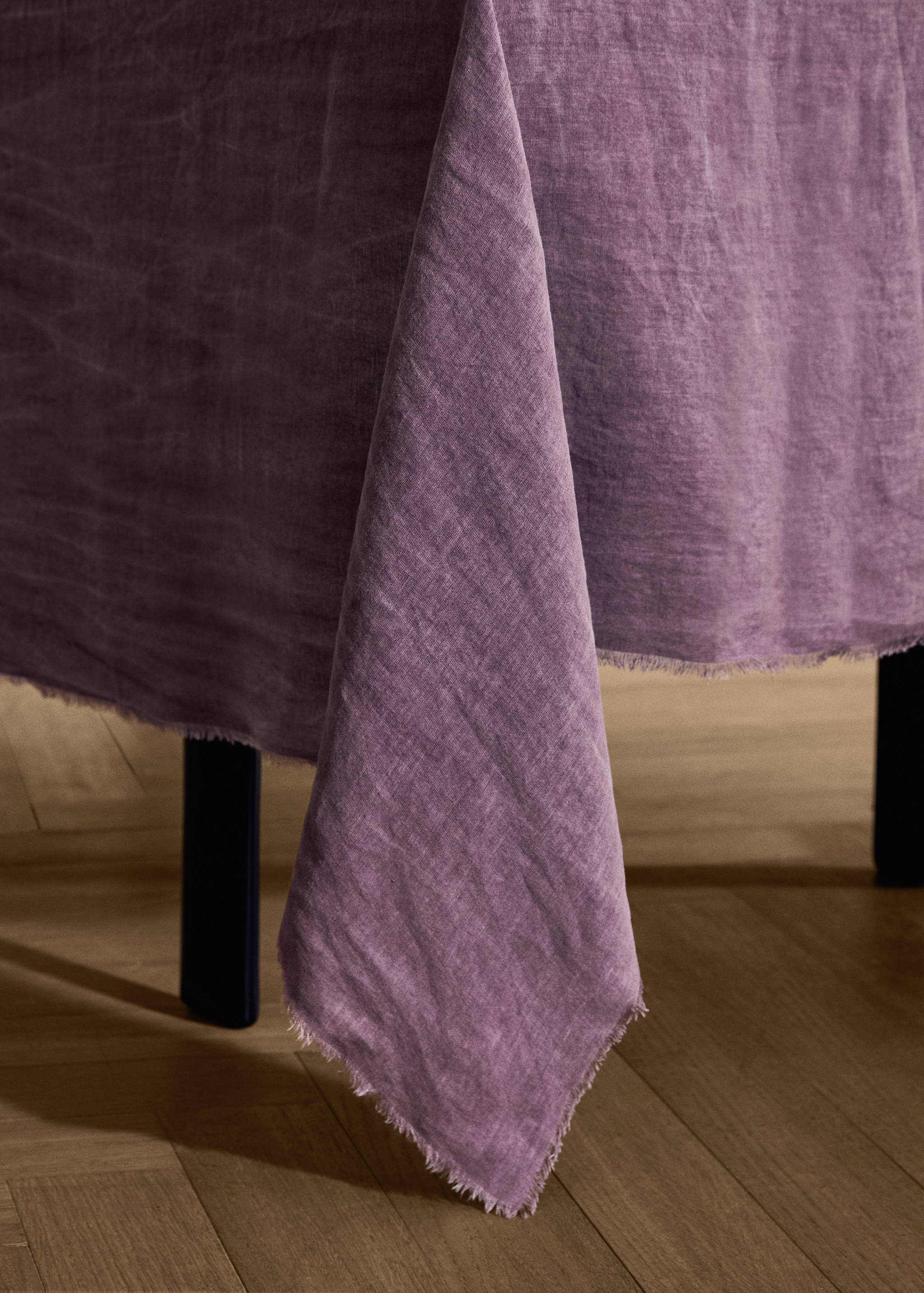 Purple linen tablecloth with frayed hem draped over a table.