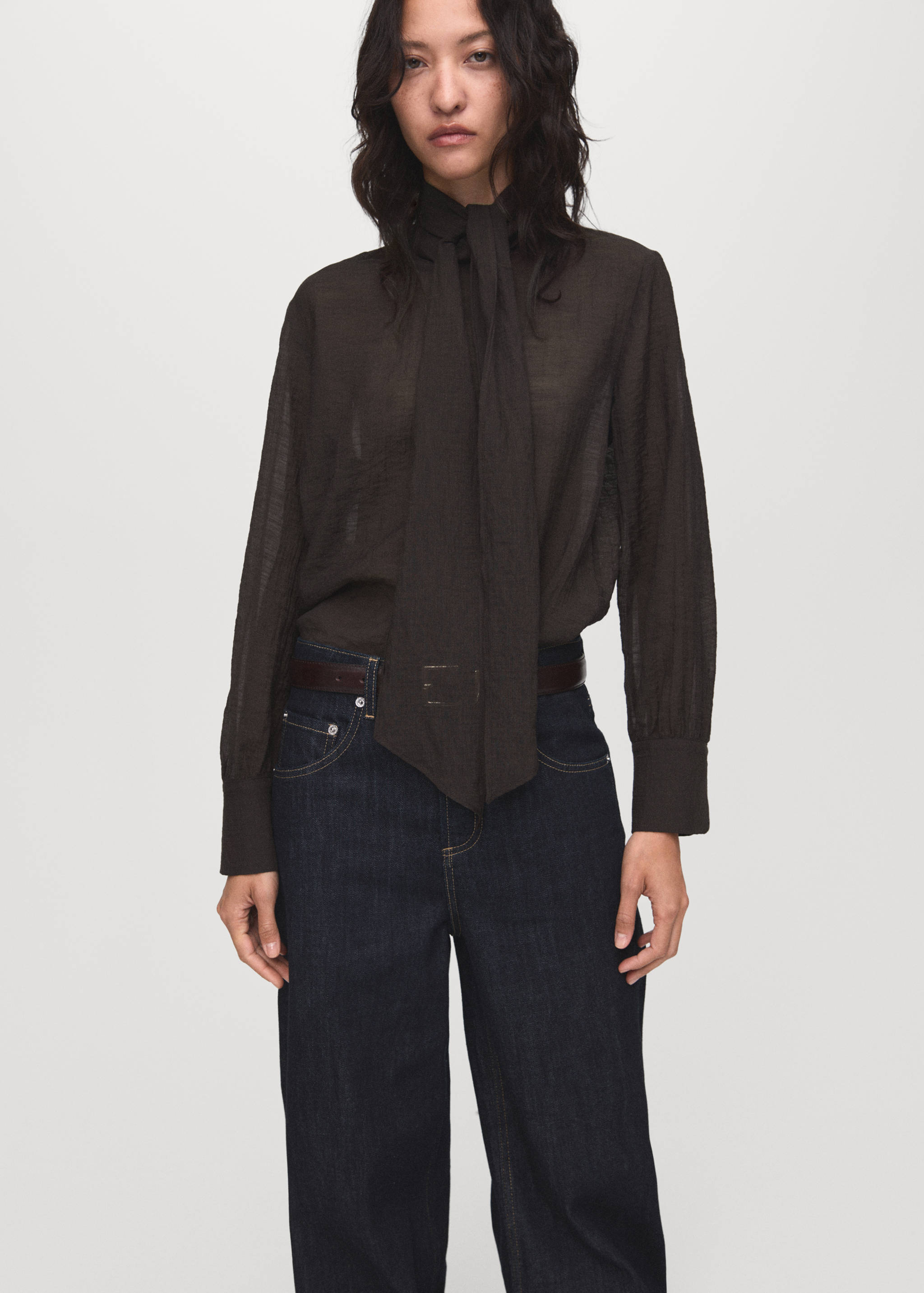 Dark brown blouse with a high neckline and neck tie, worn with dark blue denim trousers.