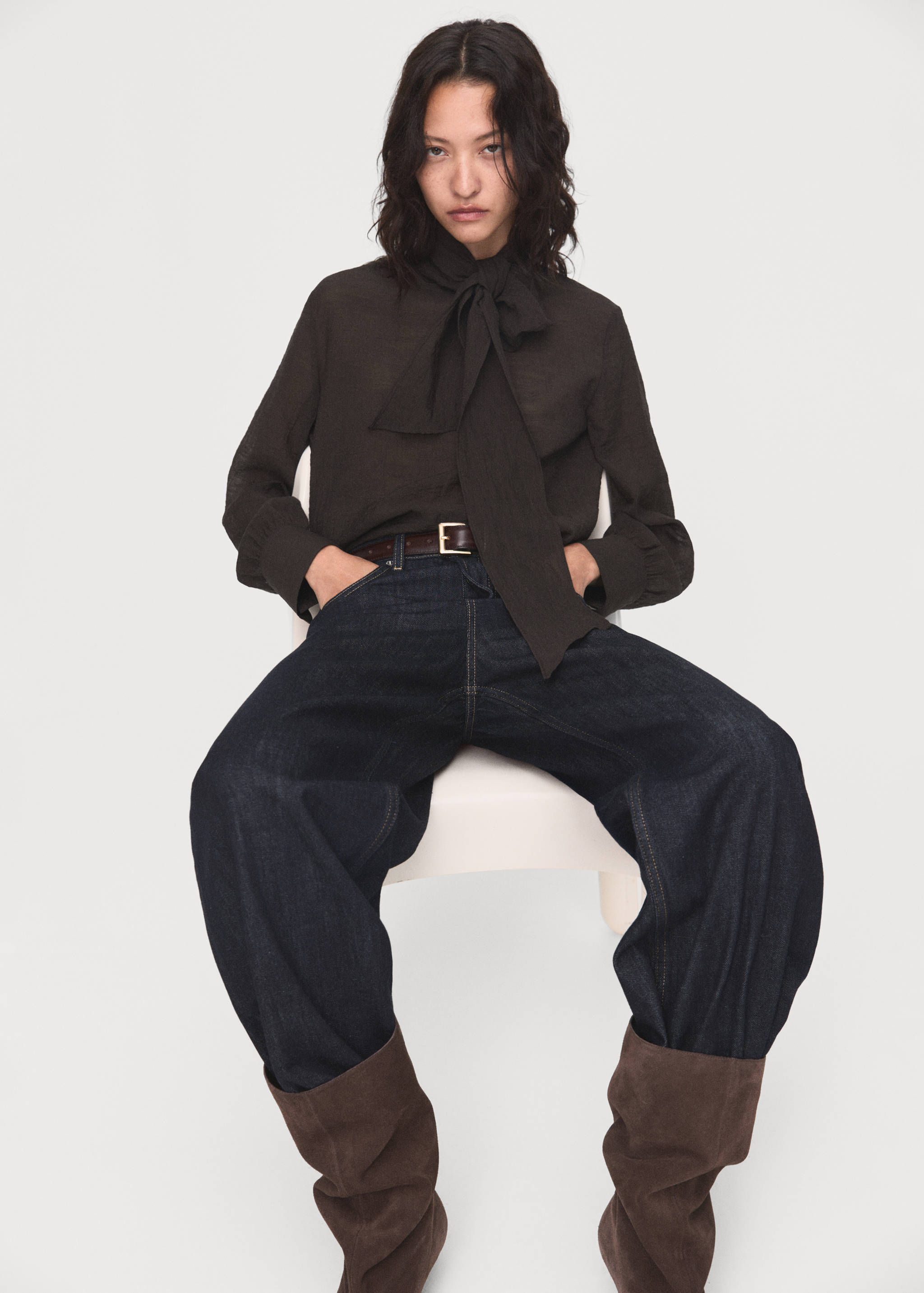 Dark brown blouse with a high neckline and neck-tie detail, worn with dark denim trousers.