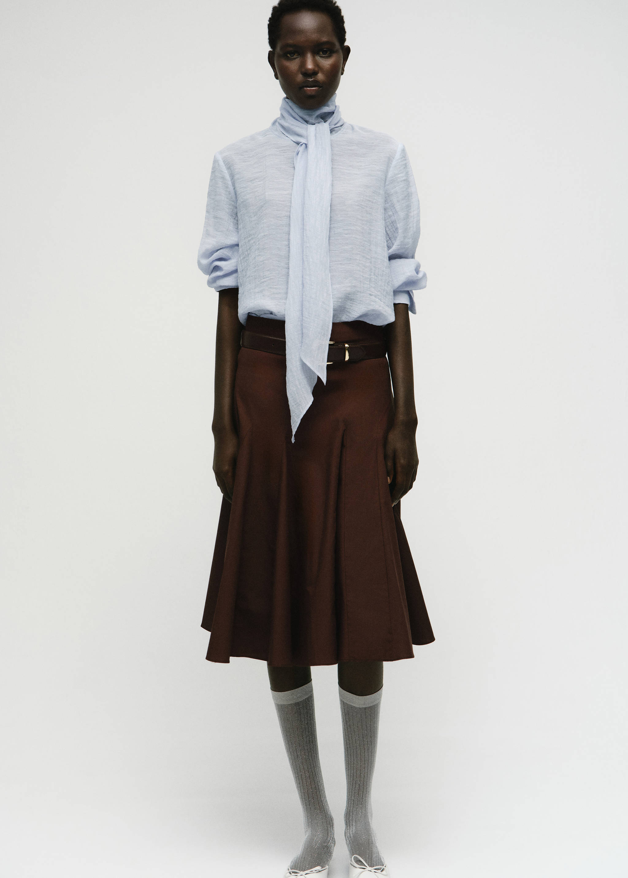 Light blue textured blouse with a tie-neck scarf, worn with a brown skirt.